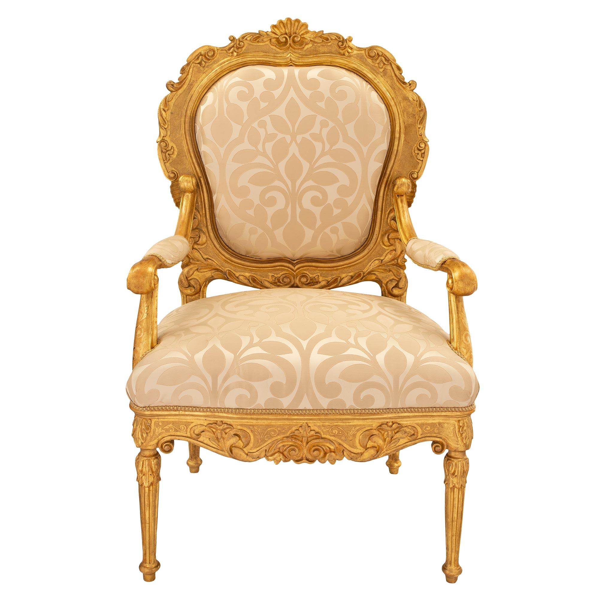 A most elegant pair of Italian 18th century Louis XV/XVI giltwood throne armchairs. Each armchair is raised by circular fluted tapered legs with top acanthus leaves. The scalloped apron has an etched scrolled design amidst carved scrolled foliate.