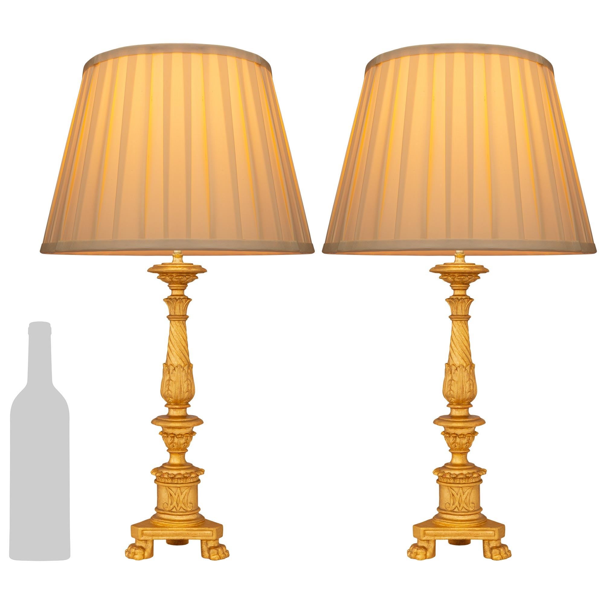 Una bella e decorativa coppia di lampade in legno dorato del periodo Luigi XVI del XVIII secolo. Ogni lampada finemente intagliata è sollevata da una base triangolare e sostenuta da tre piedi a zampa. Il futuro centrale, tornito e screziato, è