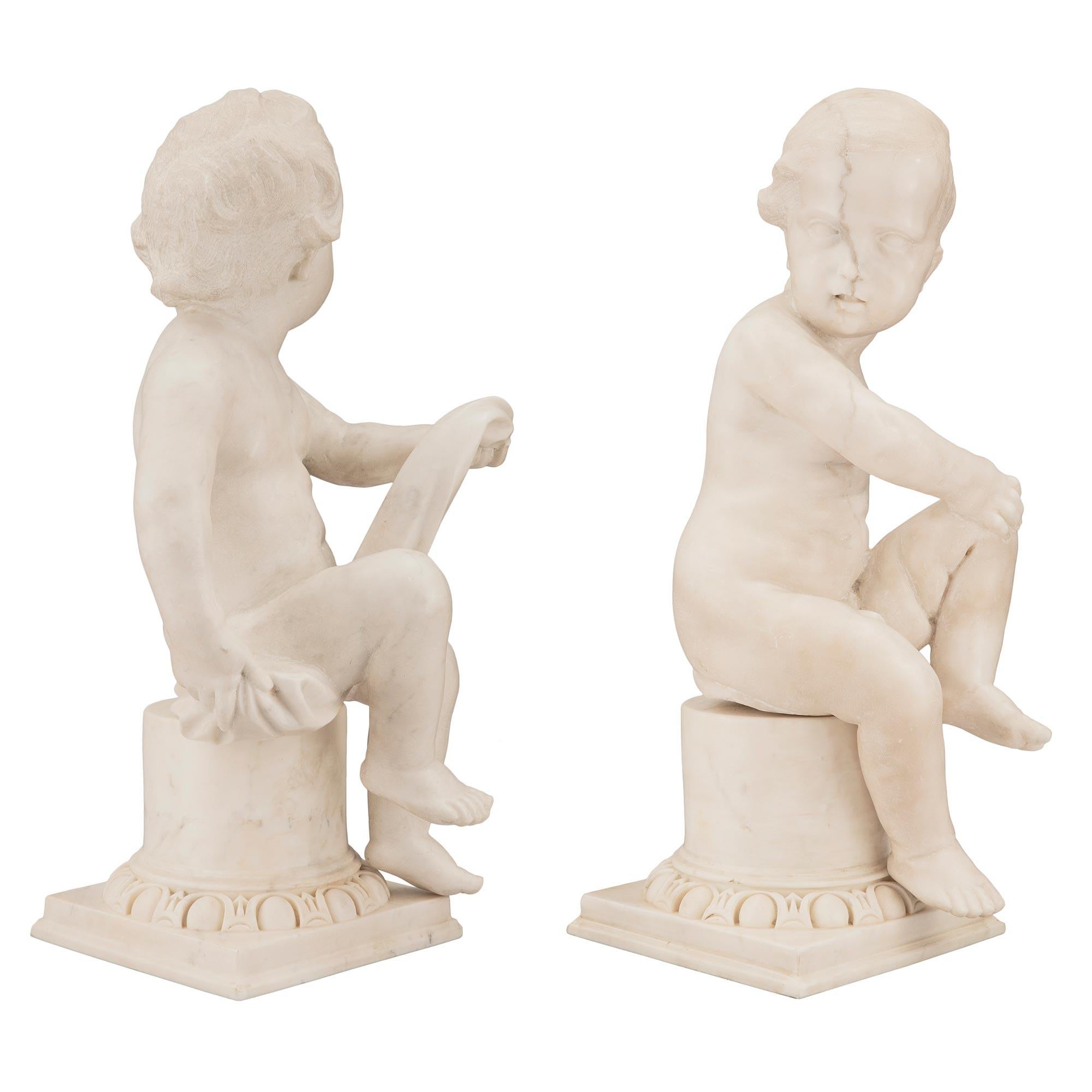 A charming true pair of Italian 18th century Louis XVI Period white carrara marble statues. Each statue is raised by a lovely square base with a Les Oves pattern and circular central support. Each charming and richly sculpted young boy is seated on