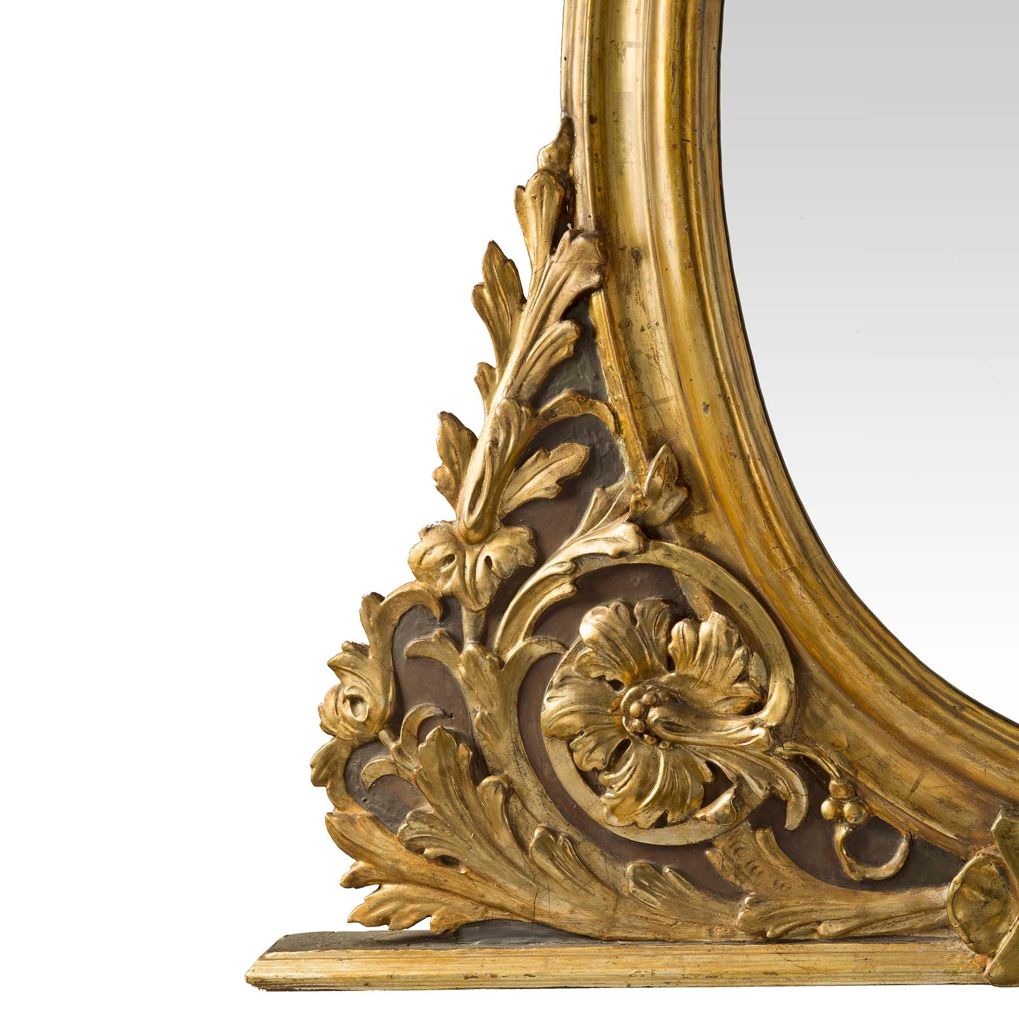An unusually shaped pair of Italian 18th century mecca and patinated mirrors. The pair with a wide mottled bottom shelf has a central shield flanked by elaborate foliate mecca scrolls. At the center are vertical oval mottled frames fitted with