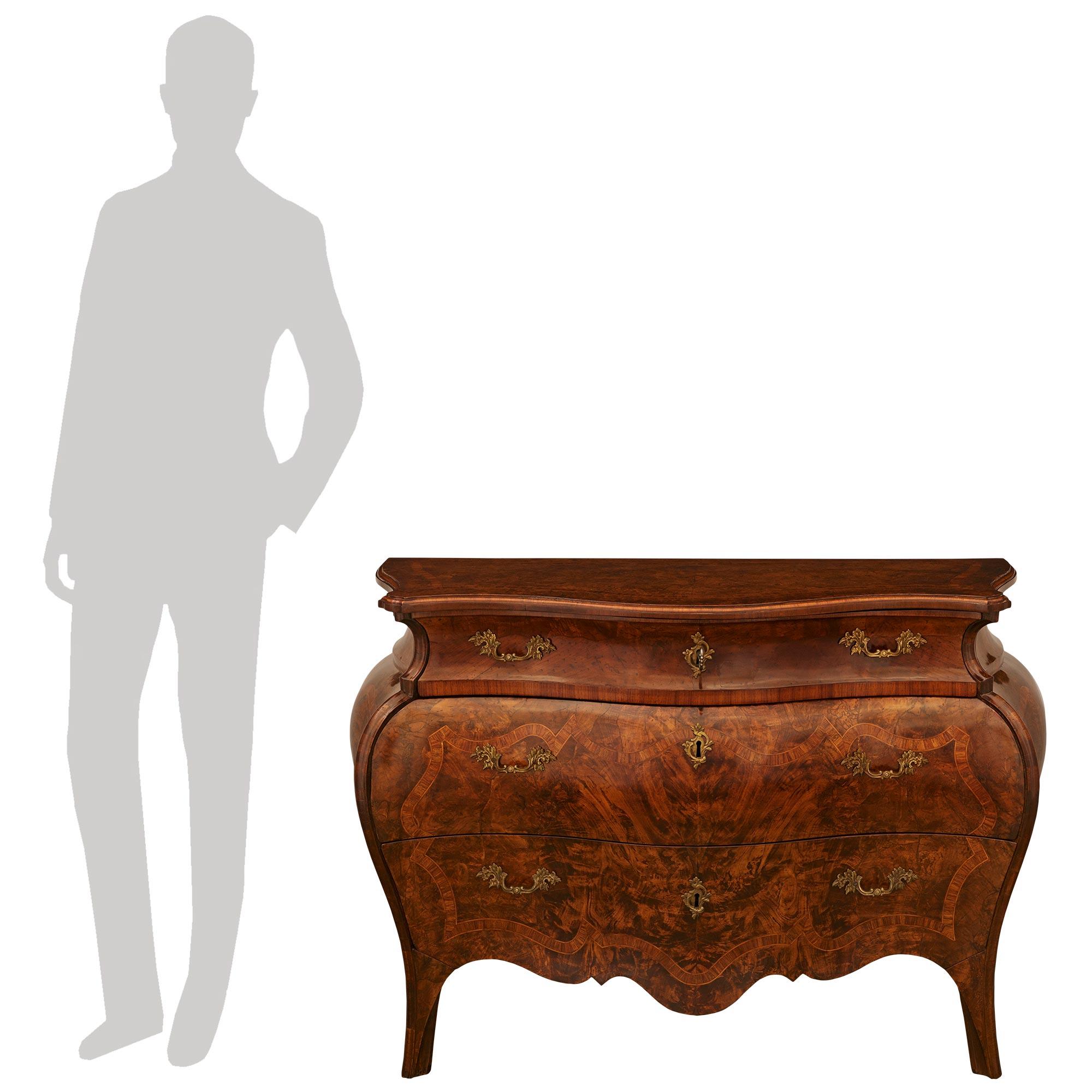 A sensational and high quality pair of Italian early 18th century Rococo Period Burl Walnut, Fruitwood and Bronze commodes. Each impressive three drawer chest displays an exaggerated Bombee shape while raised on four scrolled legs flanking the