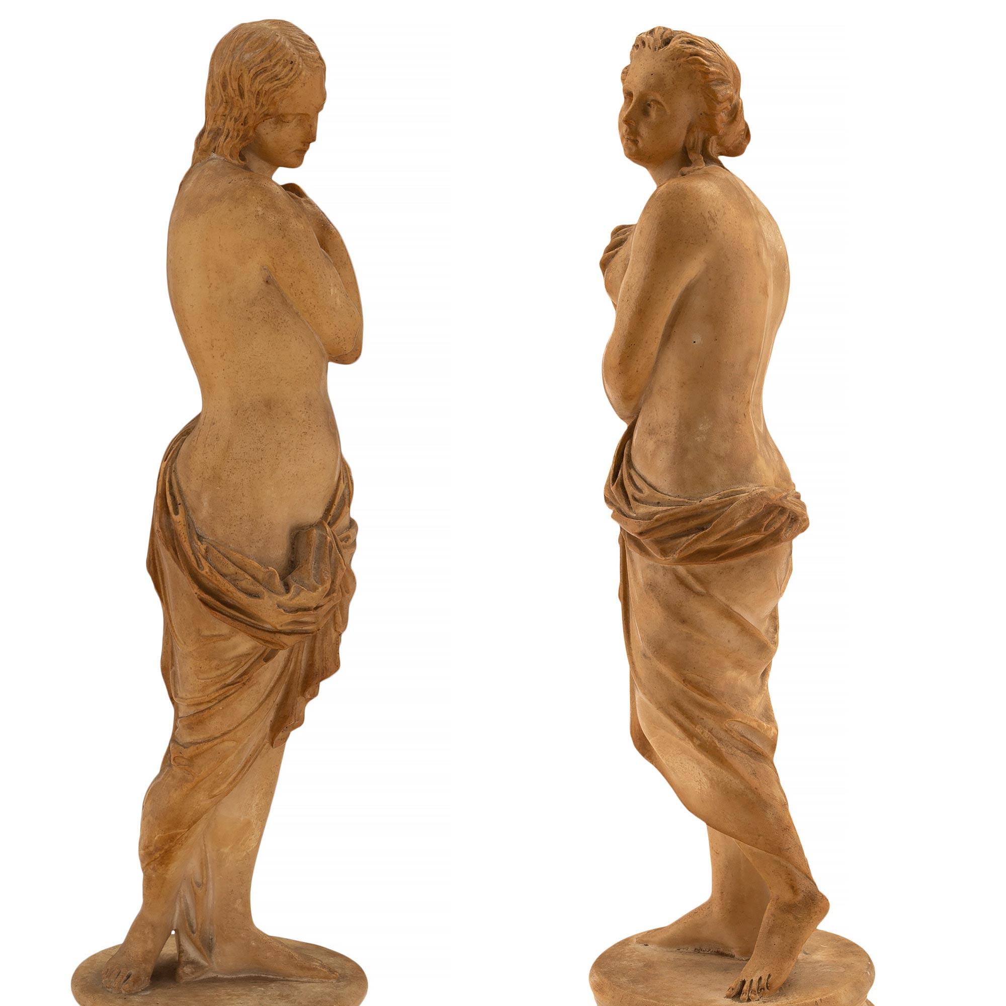 An exceptional and most charming true pair of Italian 18th century terra cotta statues. Each statue is raised by a mottled circular base where the elegant and wonderfully executed maidens stand. Each beautiful maiden is draped in detailed flowing