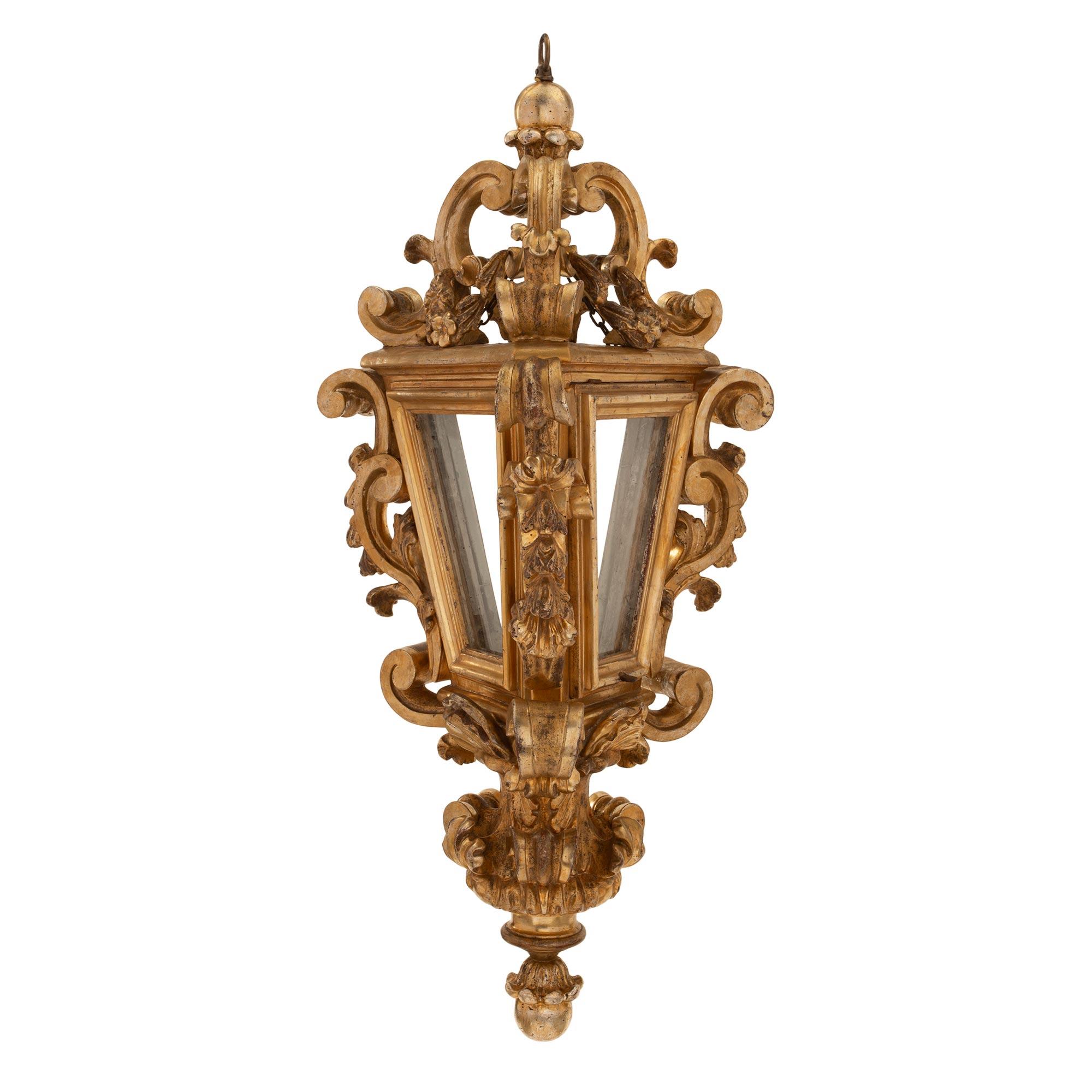 A beautiful pair of Italian 18th century Venetian Mecca lanterns. Each lantern is centered by an elegant bottom foliate finial below rich scrolled designs. The triangular shaped body retains the original glass panes flanked by finely carved and most