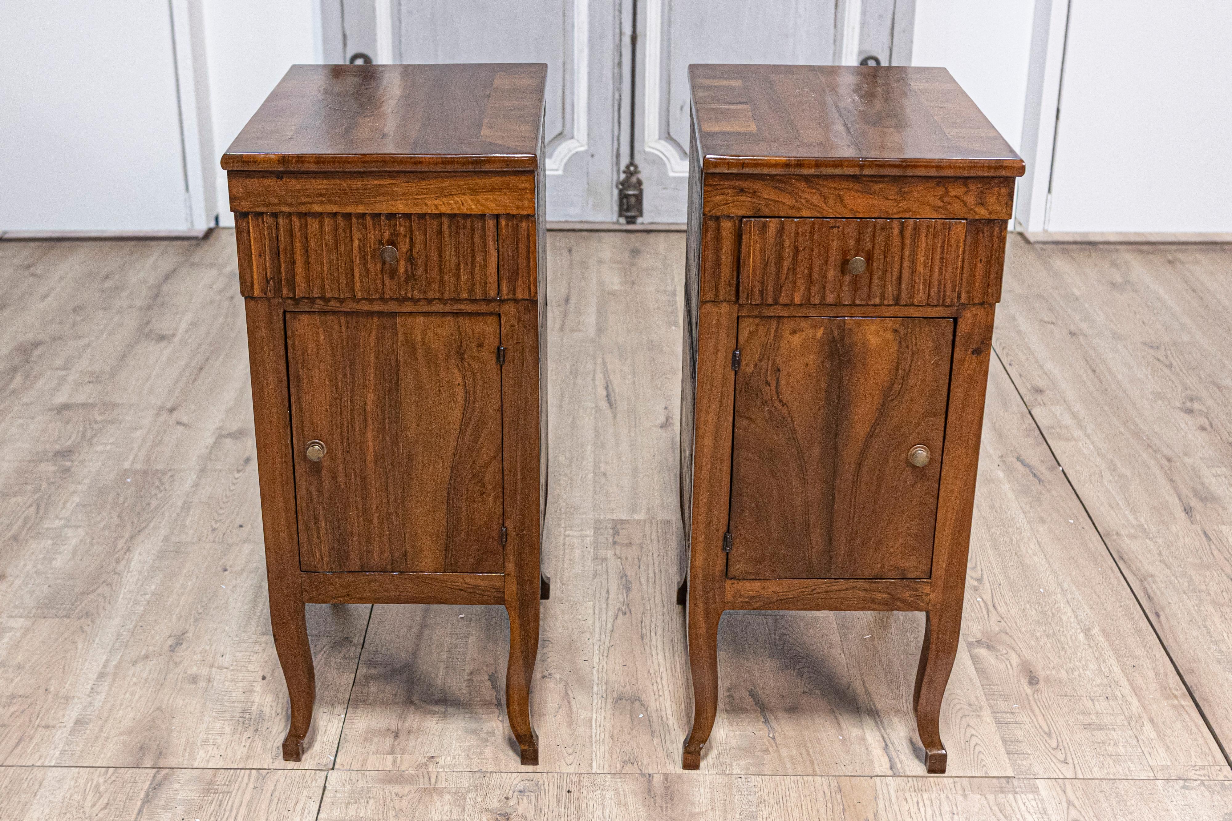 A pair of Italian walnut bedside chests from the 18th century with carved fluted drawer, single door and curving legs. This exquisite pair of Italian walnut bedside chests from the 18th century captures the elegance and craftsmanship of the period.