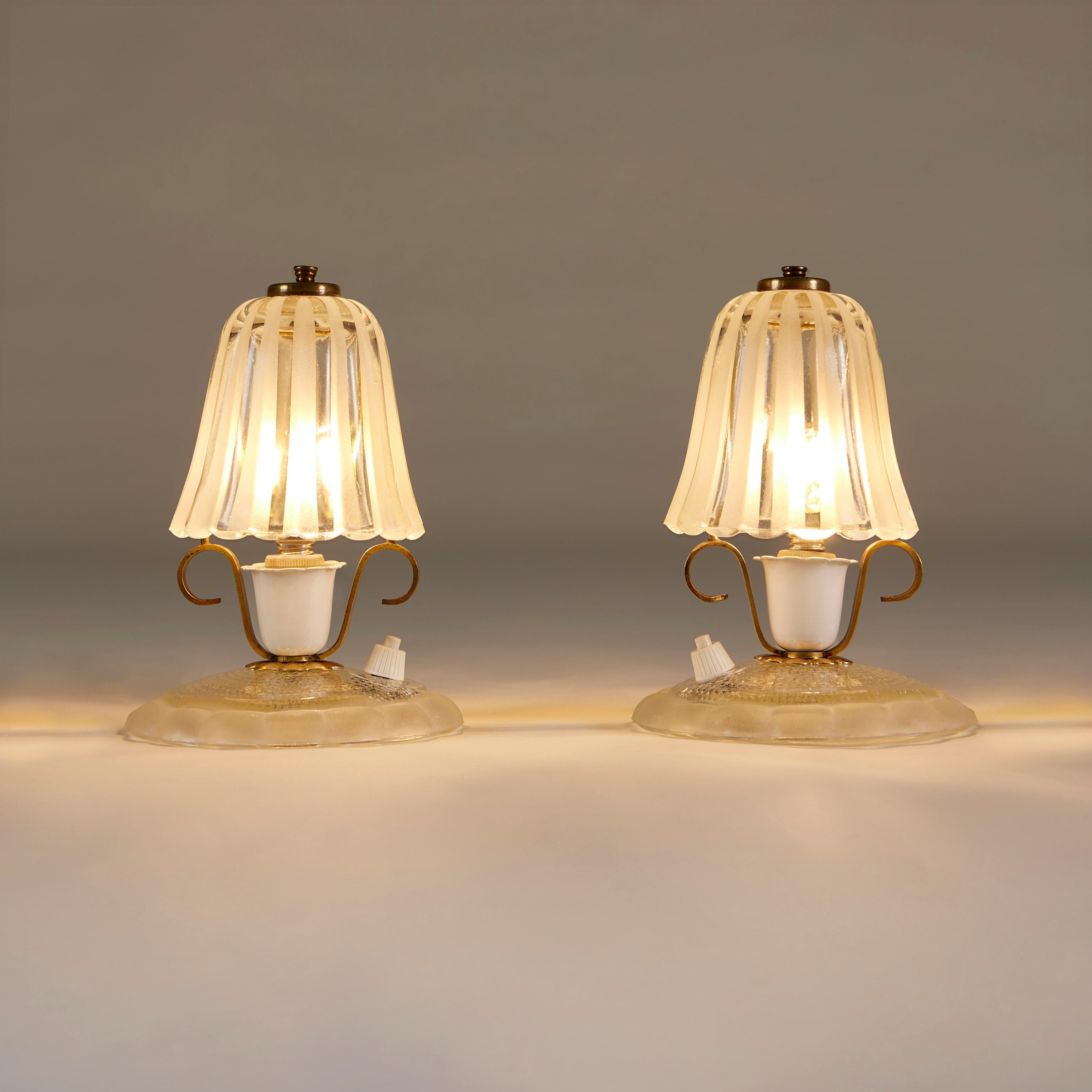 Unusual pair of shaped textured glass shades sit on circular scalloped glass base. Decorative brass accent details. Perfect for a dressing-table or desk or anywhere in need of a mood enhancing touch.
