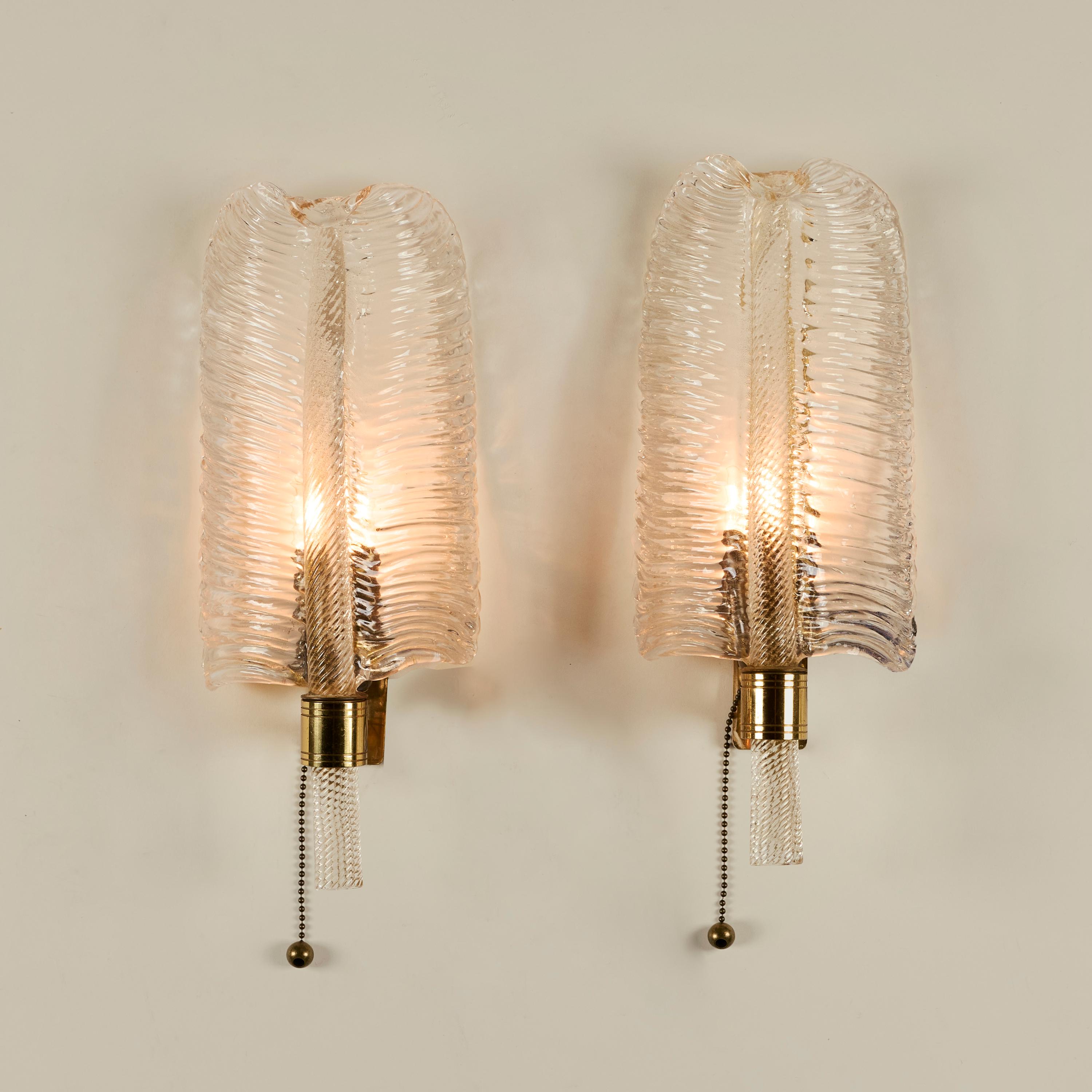 Elegante coppia di applique a foglia in vetro di Murano degli anni '50. Ciascuna lampada è soffiata a mano per creare una texture di foglie sottilmente dorate, con la parte superiore tornita e sostenuta da uno stelo a torchon dorato. Raccordi e
