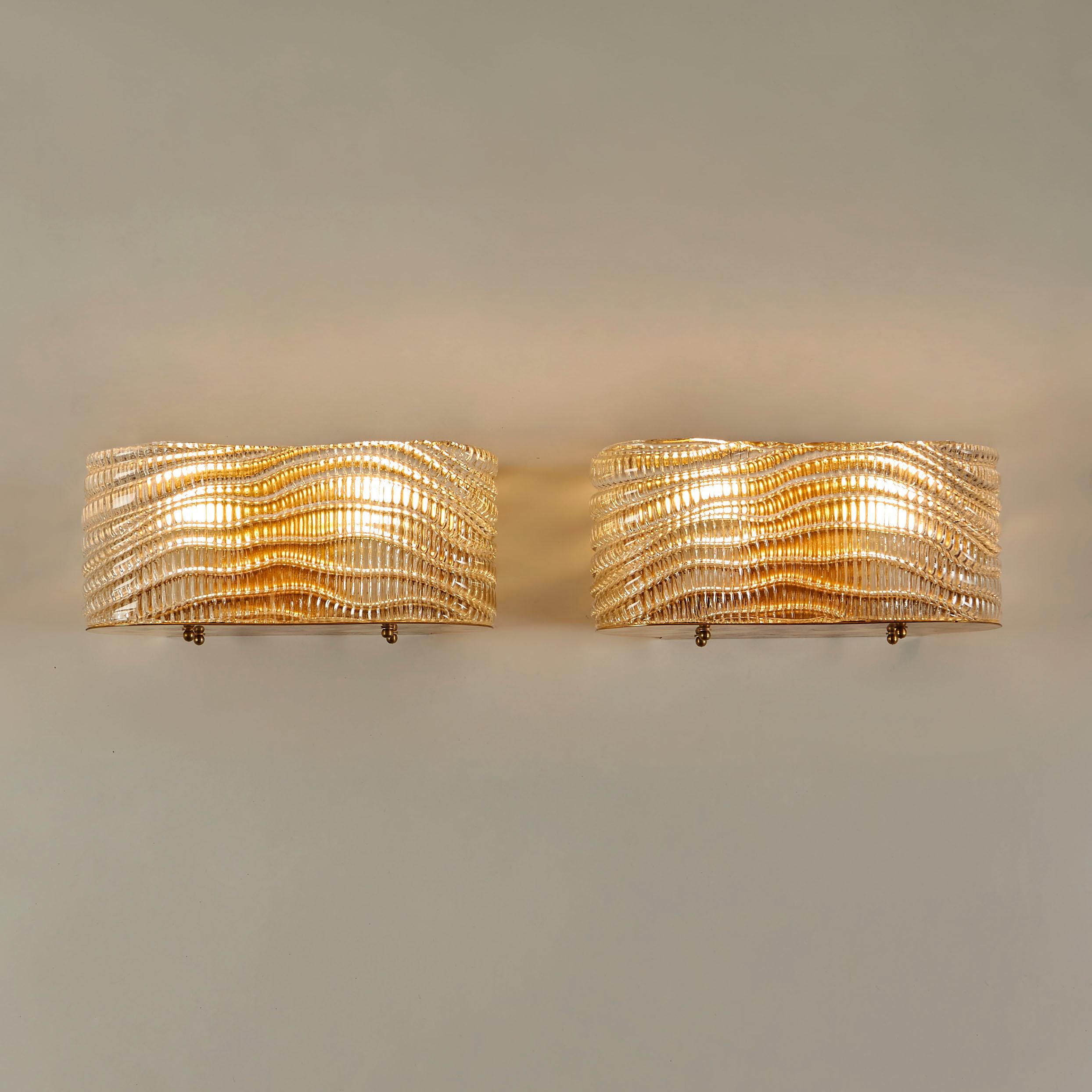 Pair of glamorous curved wall lights. Textured Murano glass with diagonal swirl detailing sit on curved brass base.The reflection of textured glass and rich brass creates a flattering diffused light.
 