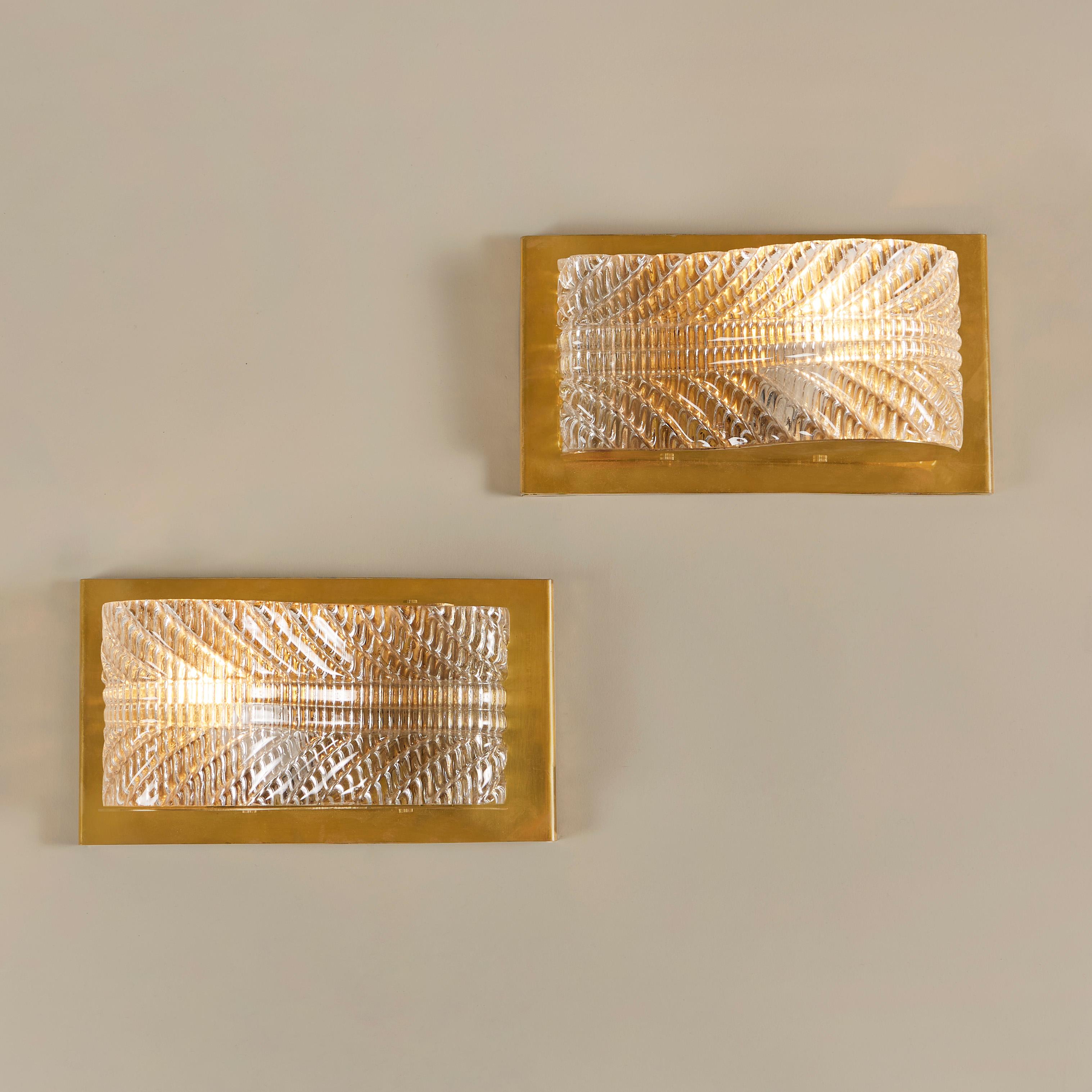 Ein Paar glamouröse geschwungene Wandleuchten. Texturiertes Murano-Glas mit eleganten Details sitzt auf einer rechteckigen Messinggrundplatte. Die Reflexion von strukturiertem Glas und reichem Messing erzeugt ein schmeichelhaftes, diffuses Licht.
