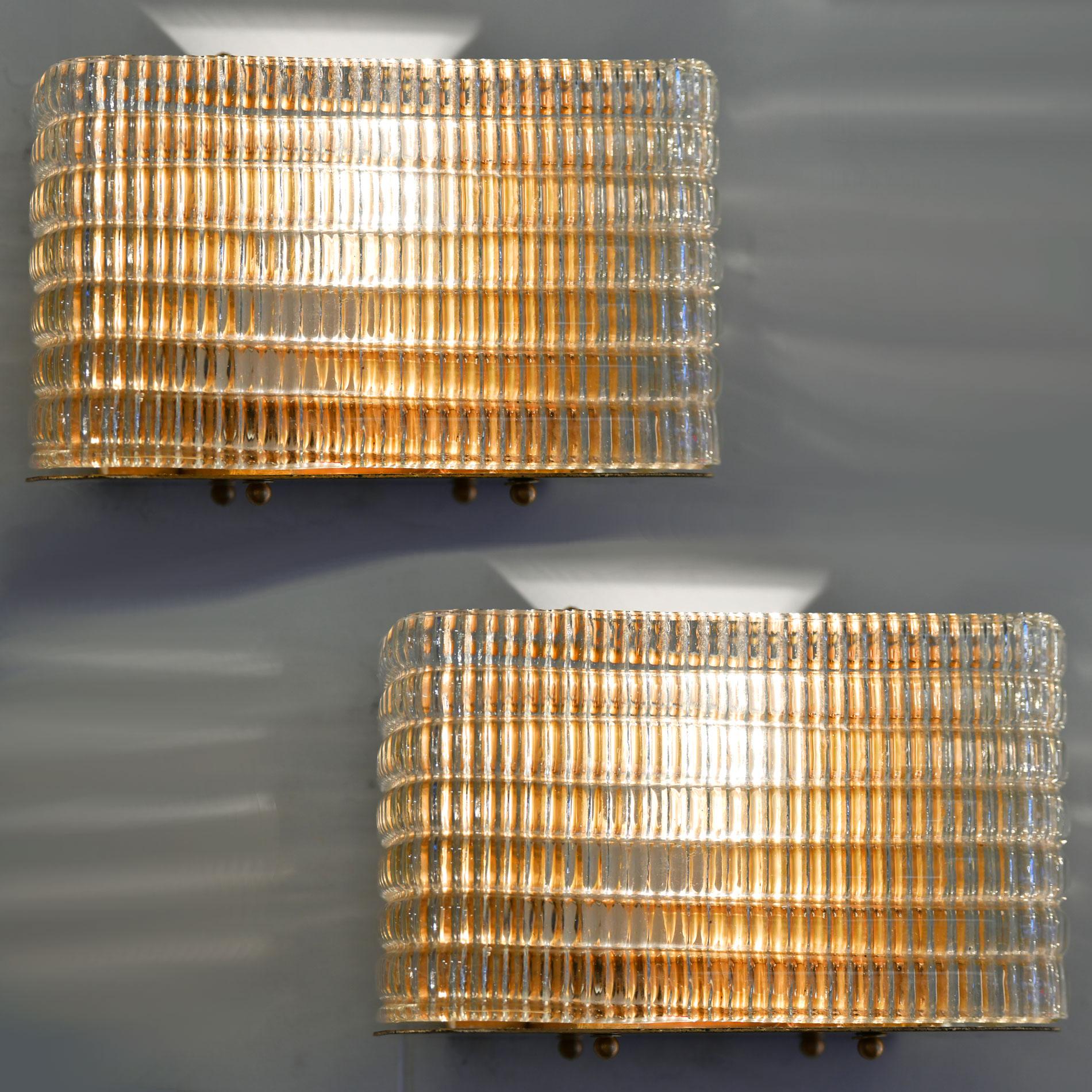 Glamorous wall light with curved corners. Six layers of textured glass, the vertical ribbing effect is on the inside whilst the outside is horizontal shape in layers. The overall effect of the glass alongside the reflection of the brass back plate