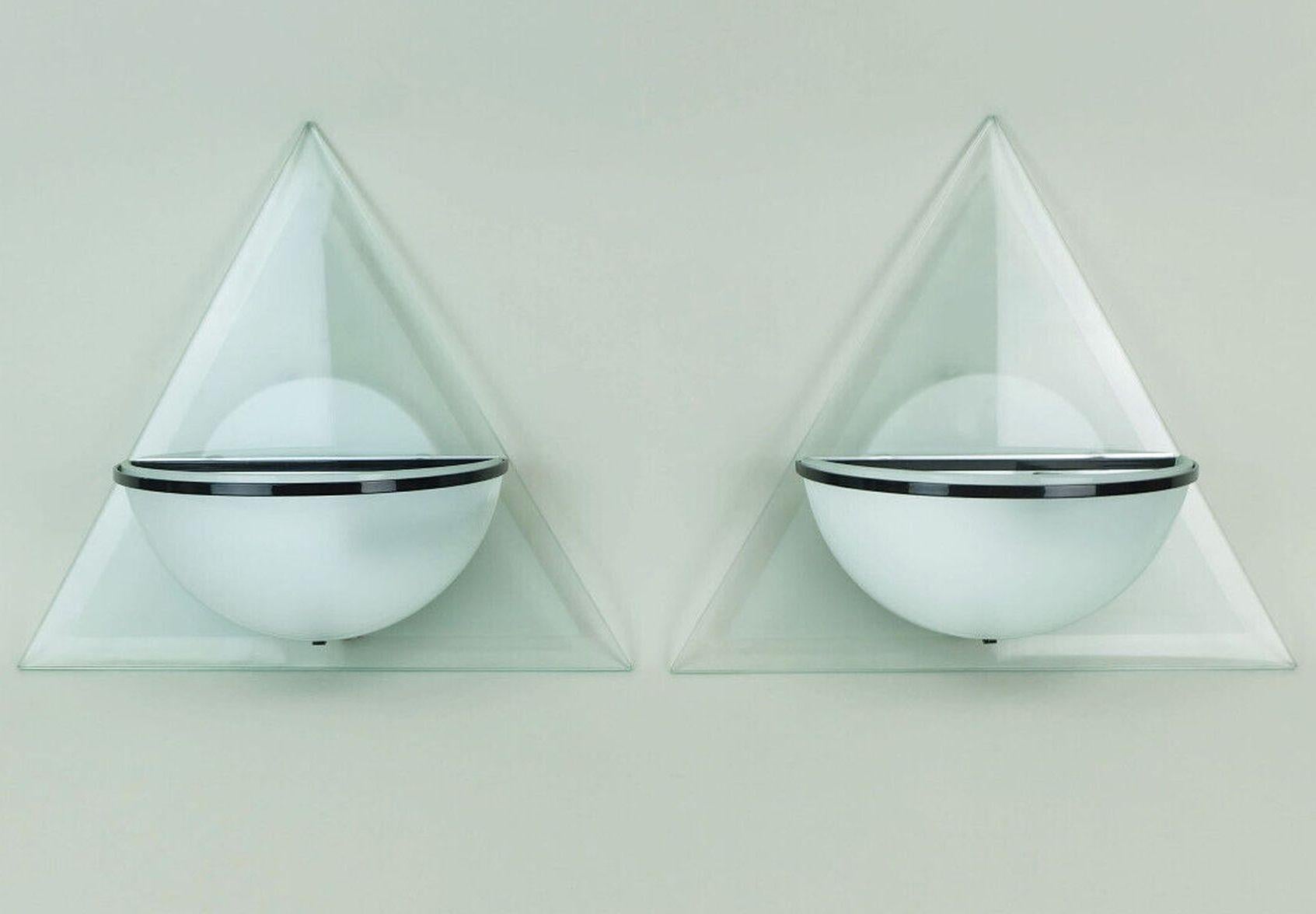 Un par de apliques de la década de 1980 fabricados por Lamperti, modelo Illo, diseño Alberto Podestà. Respaldo triangular y pantalla en forma de media concha de cristal grabado, ligeramente verdoso y brillante. Soporte de pantalla de metal negro