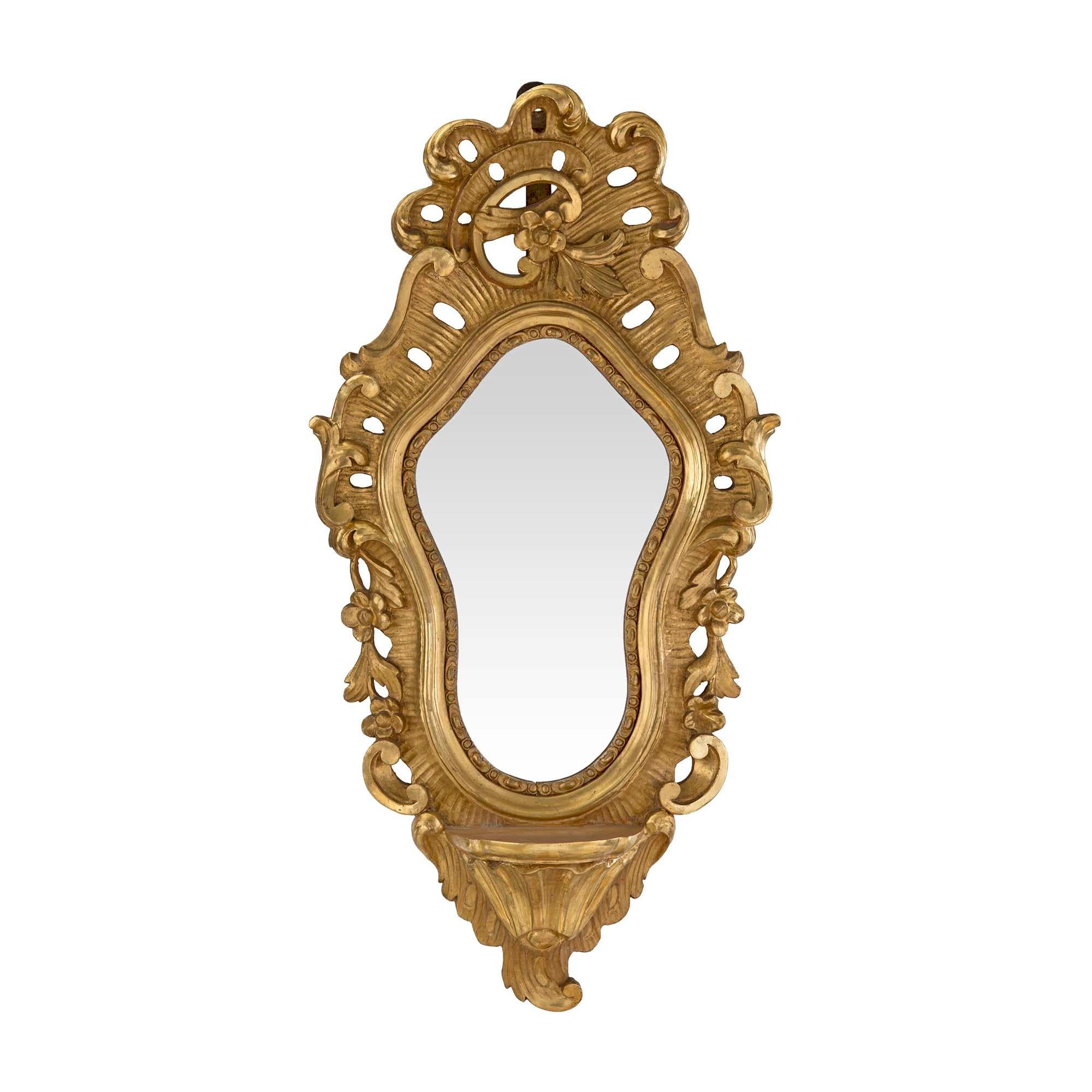 A stunning pair of Italian 19th century Baroque mirrored giltwood wall brackets. The finely carved wall brackets have a shelf at the bottom. Scrolls and foliate designs decorate the pierced frame centered by a lovely contoured mirror. With a