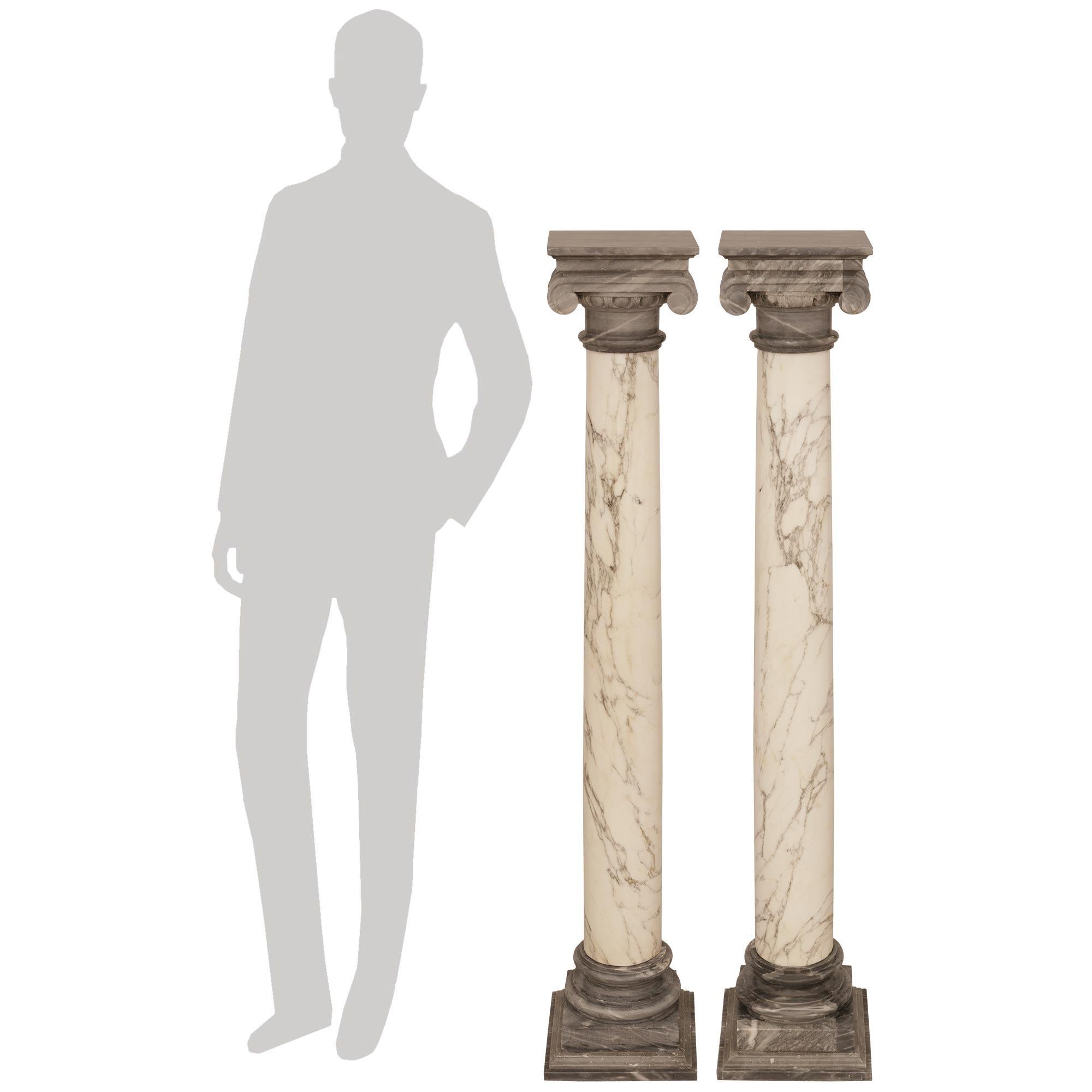 A decorative pair of Italian 19th century Calacatta and Gris St. Anne marble pedestals/columns. Each elegant column is raised on a square mottled Gris St. Anne marble plinth below a round mottled socle, with the solid Calacatta marble columns above.