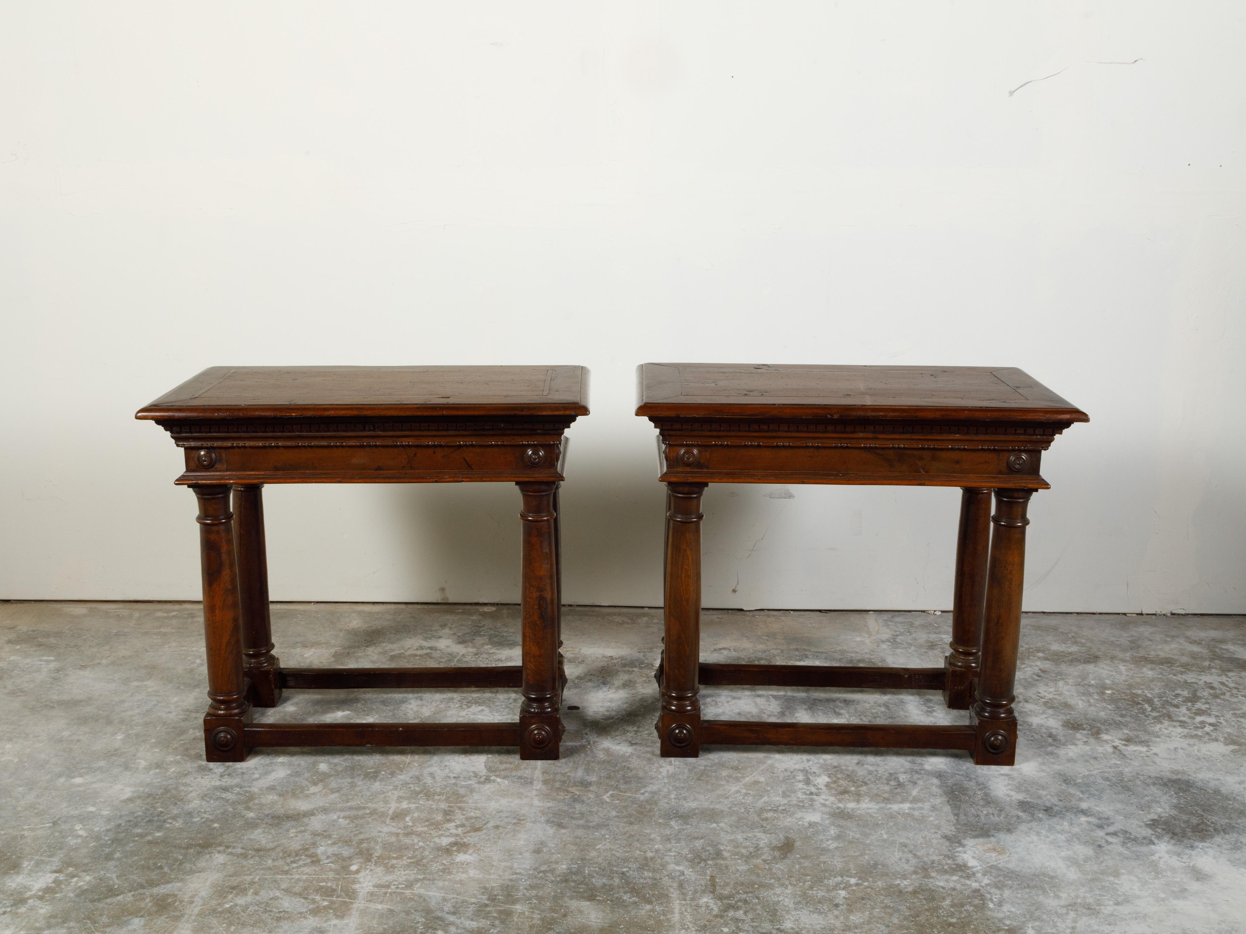 A Pair of Italian walnut console tables from the 19th century, with carved dentil molding and Doric columns. Created in Italy during the 19th century, each of this pair of walnut console tables features a rectangular top with beveled edges, sitting