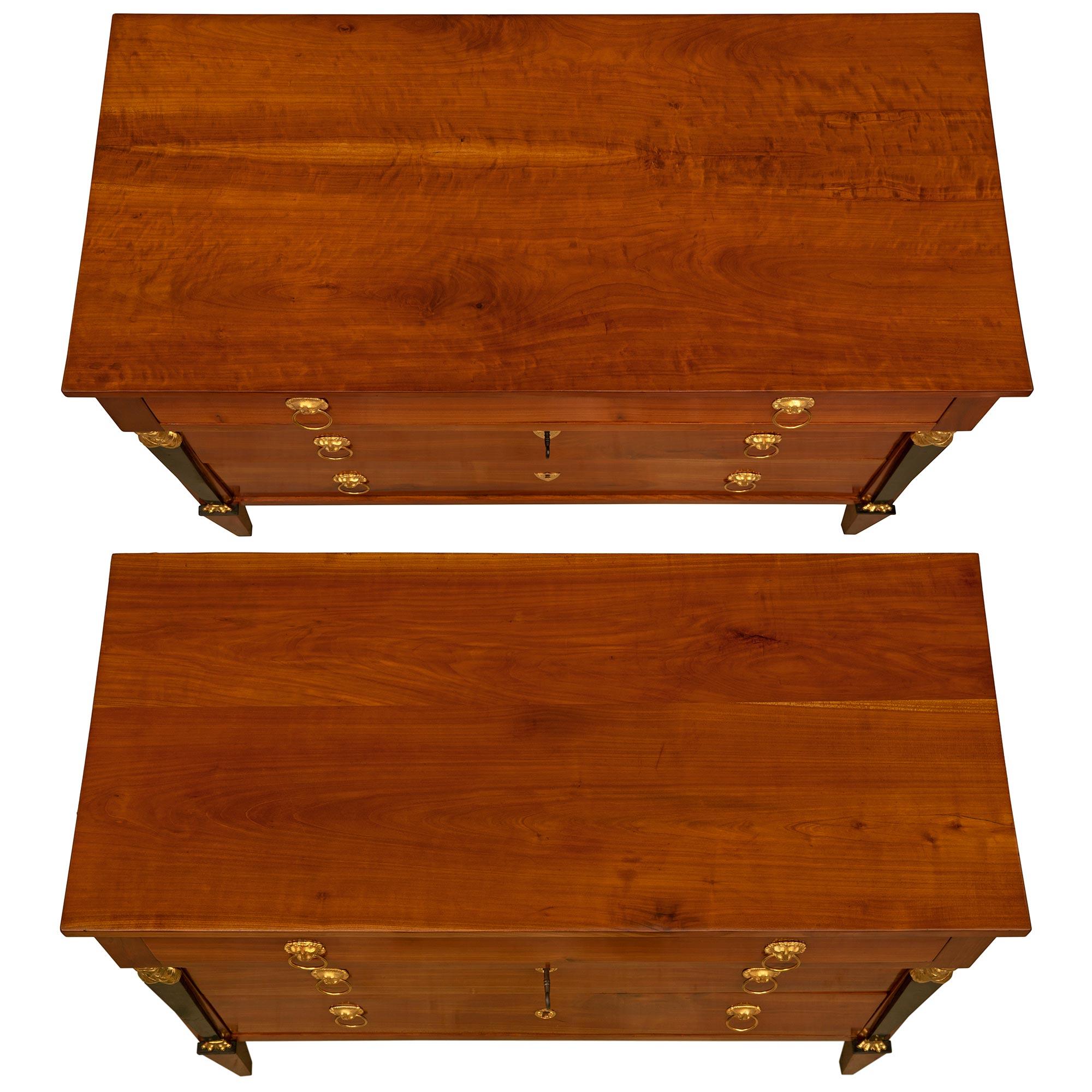 A striking pair of Italian 19th century Empire st. Cherrywood, ebonized Fruitwood and ormolu commodes. Each three drawer chest is raised by elegant square tapered legs below remarkable ebonized fruitwood tapered columns with richly chased ormolu