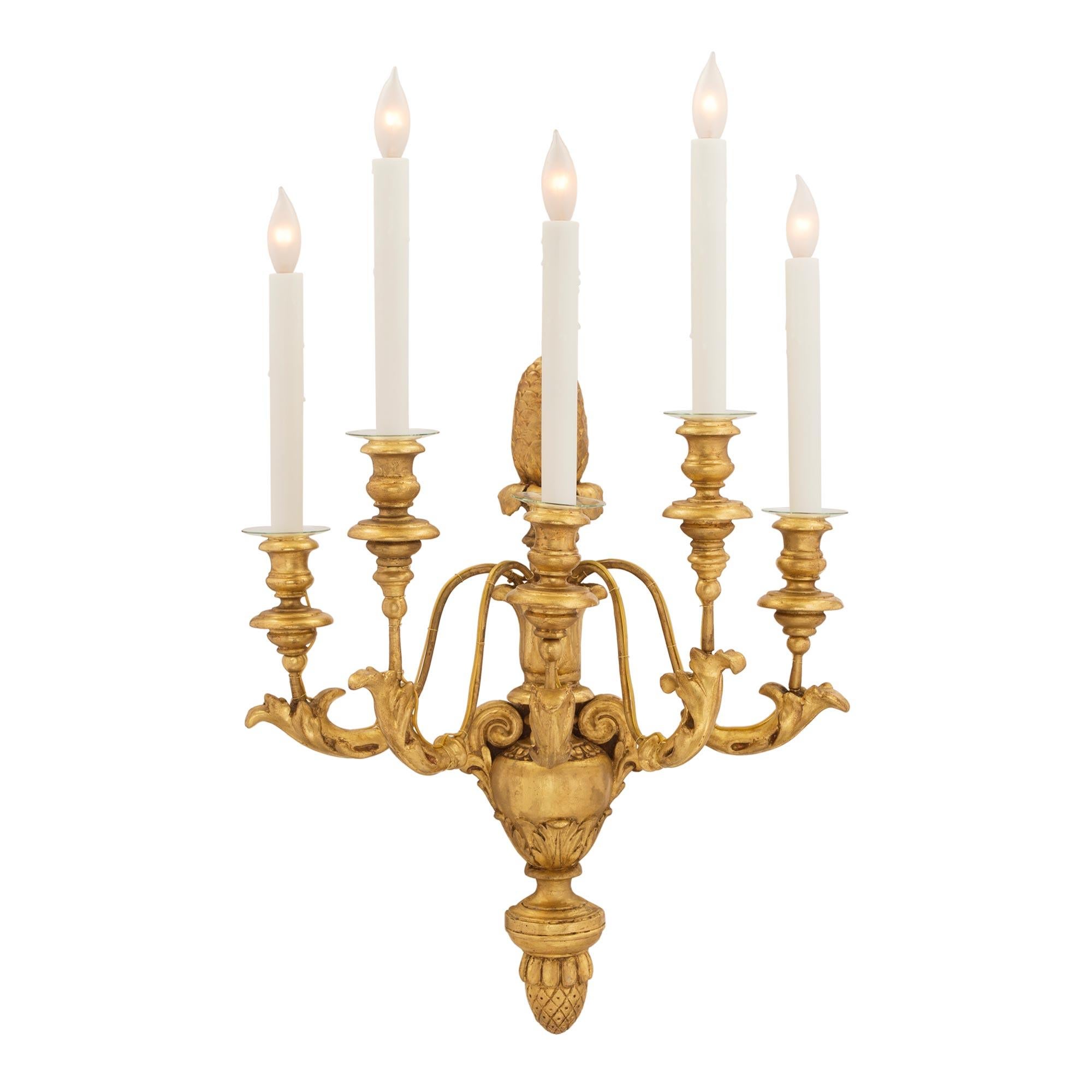 Ein schönes Paar italienischer fünfarmiger vergoldeter toskanischer Wandleuchter aus dem 19. Jede Leuchte wird von einer fein geschnitzten Eichel mit einer dekorativen Urne in der Mitte gekrönt. Die eleganten S-förmig geschwungenen Arme sind mit
