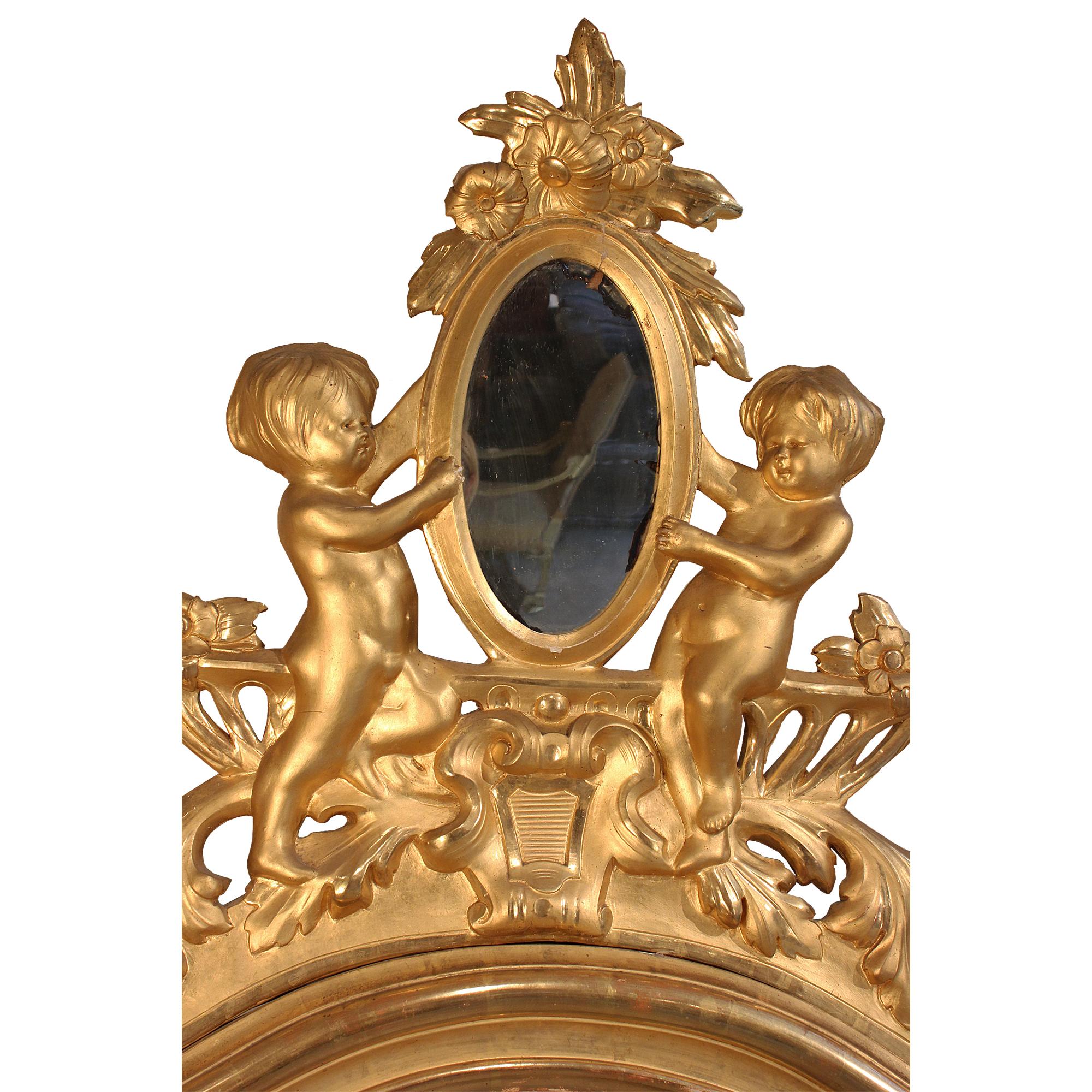 Une paire spectaculaire de miroirs italiens en bois doré du 19ème siècle. Les miroirs rectangulaires à encadrement mouluré, à plateau incurvé et réserve centrale ajourée, sont ornés de deux charmants angelots présentant un miroir ovale à fleurs.