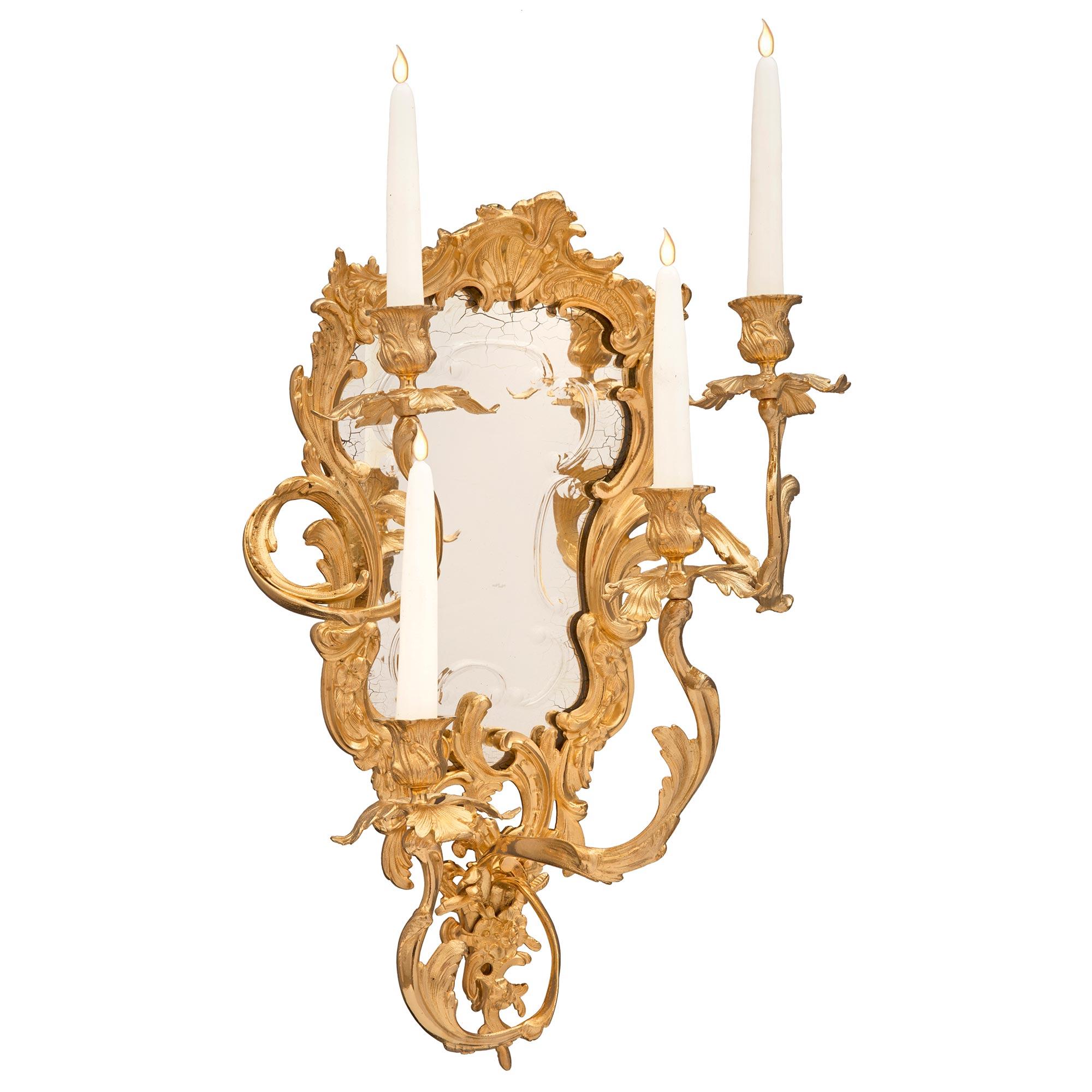 A striking and extremely decorative true pair of Italian 19th century Louis XV st. ormolu mirrored Venetian sconces. Each four arm sconce is centered by a beautiful finely detailed pierced foliate design which extends upwards and throughout the
