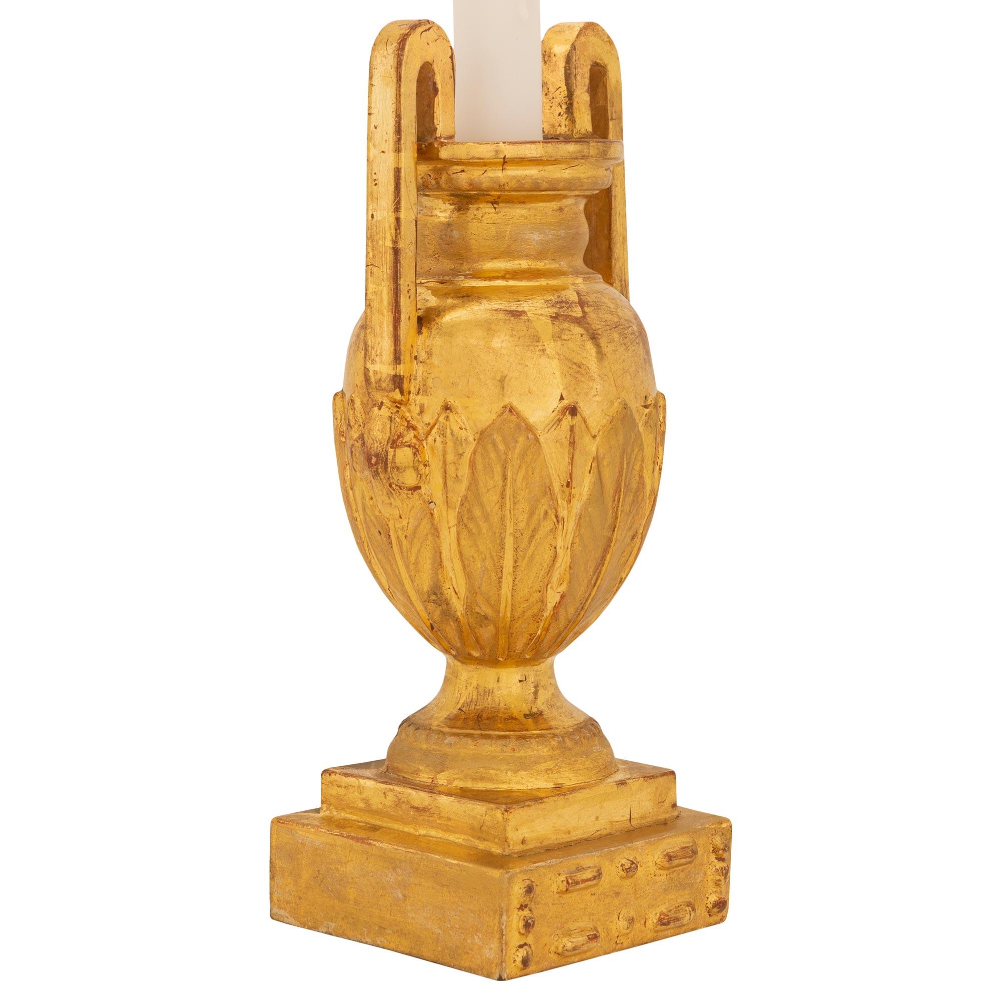 Une charmante paire de lampes italiennes du 19ème siècle en bois doré de style Louis XVI. Chaque lampe est surélevée par une base carrée avec des motifs perlés finement sculptés sous le support du piédestal en forme de socle. L'élégant corps en