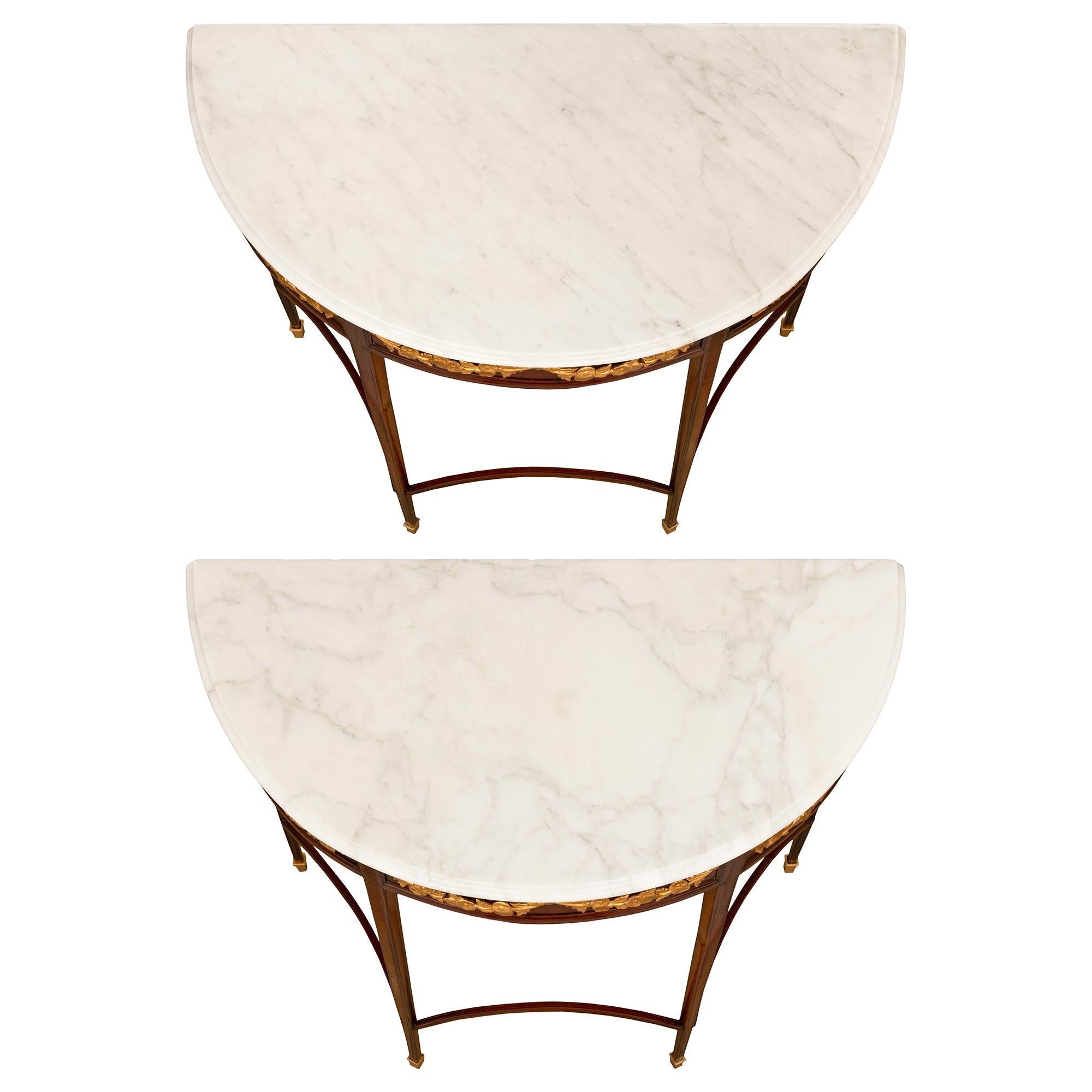 A most elegant pair of Italian 19th century Louis XVI st. Mahogany, Giltwood, Ormolu and white Carrara marble consoles. The pair of freestanding 'D' shaped consoles are raised on four square tapered legs with mottled corners and ending with Ormolu