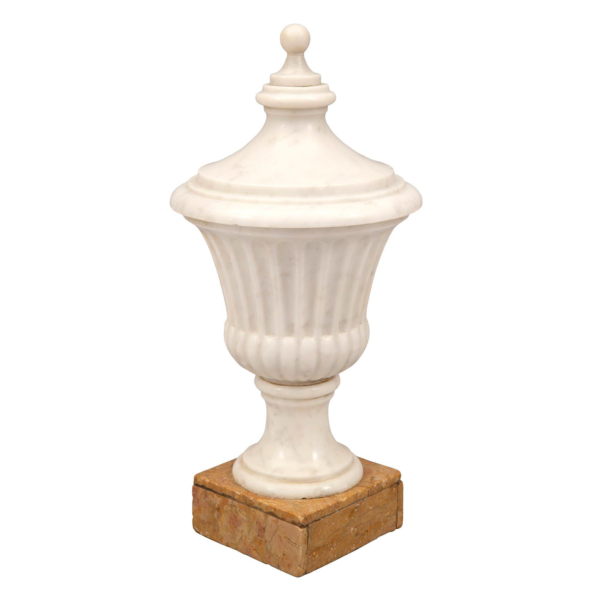 A lovely pair of Italian mid 19th century neo-classical st. decorative white Carrara and Sienna marble urns. Each urn is raised by a square Sienna marble base below the circular mottled socle pedestal. The white Carrara marble urn displays a fine