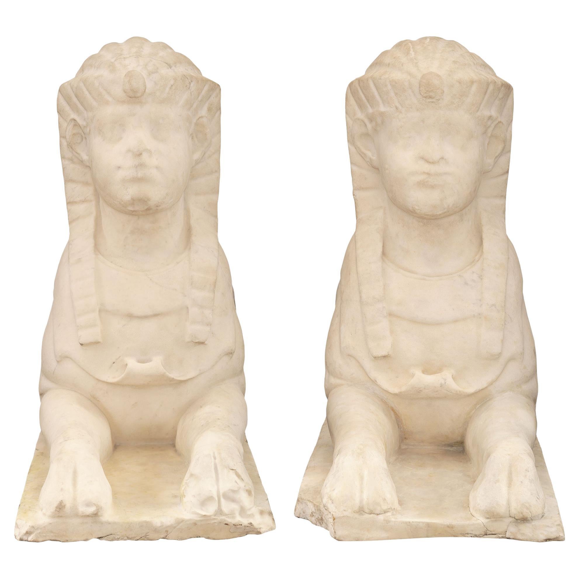 Ein beeindruckendes Paar italienischer neoklassischer Statuen aus weißem Carrara-Marmor aus dem 19. Jahrhundert, die ägyptische Sphingen darstellen. Jede Sphinx ist aus einem einzigen Stück Marmor gemeißelt und wird von einem rechteckigen Sockel