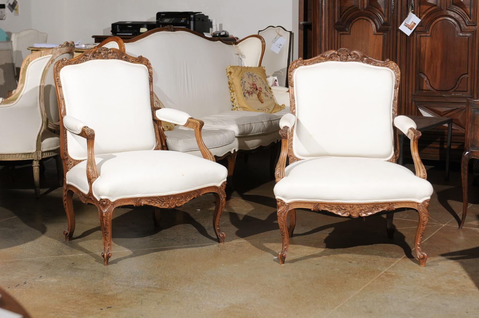 A pair of Italian Rococo style walnut armchairs from the 19th century, with carved skirts, cabriole legs and upholstery. Born in Italy during the 19th century, each of this pair of Rococo style armchairs features a slightly slanted back, adorned
