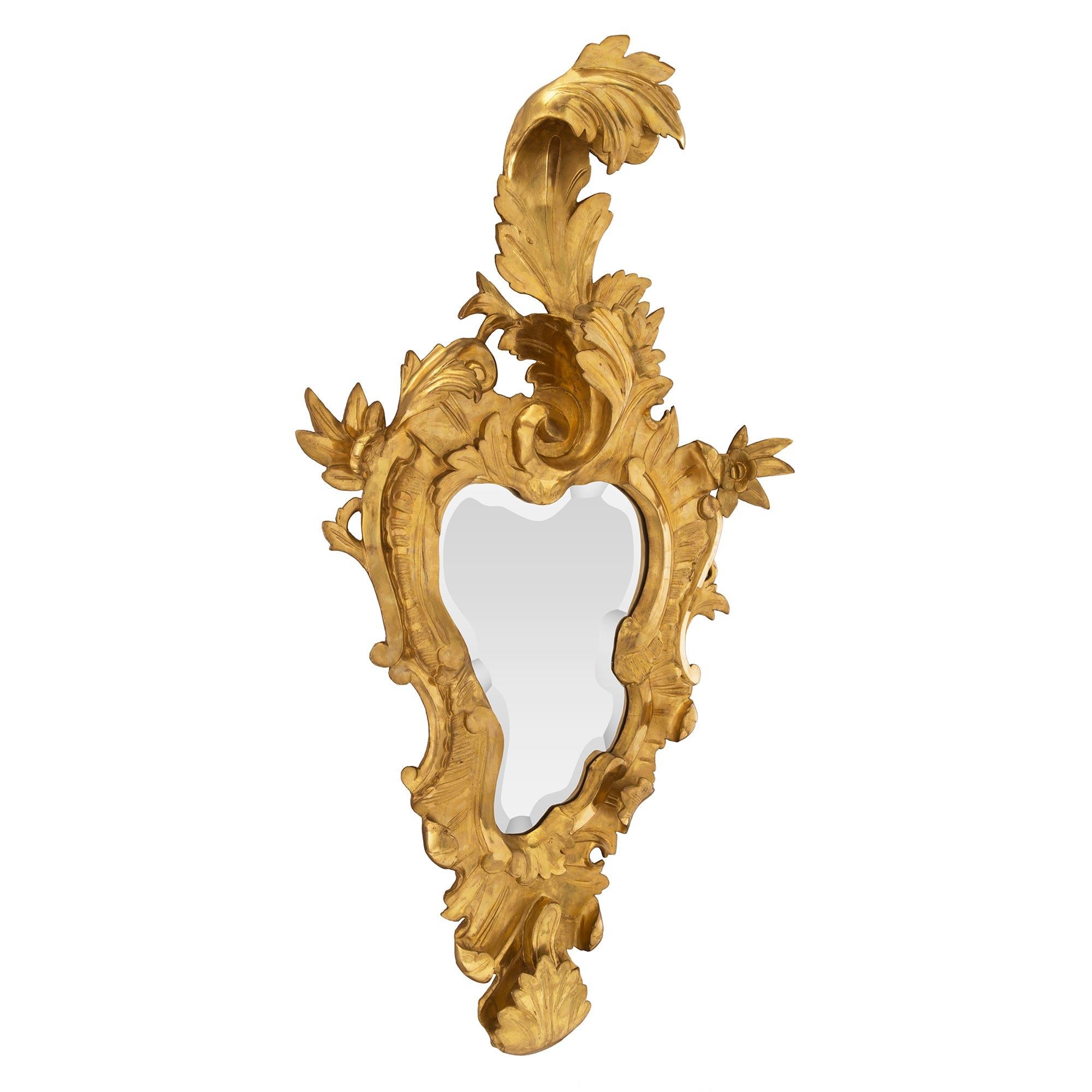 A sensational and true pair of Italian 19th century giltwood Venetian mirrors. Each beveled mirror displays the original mirror plate and follows the contour of the finely carved giltwood frame. The frame displays a rich array of scrolling patterns