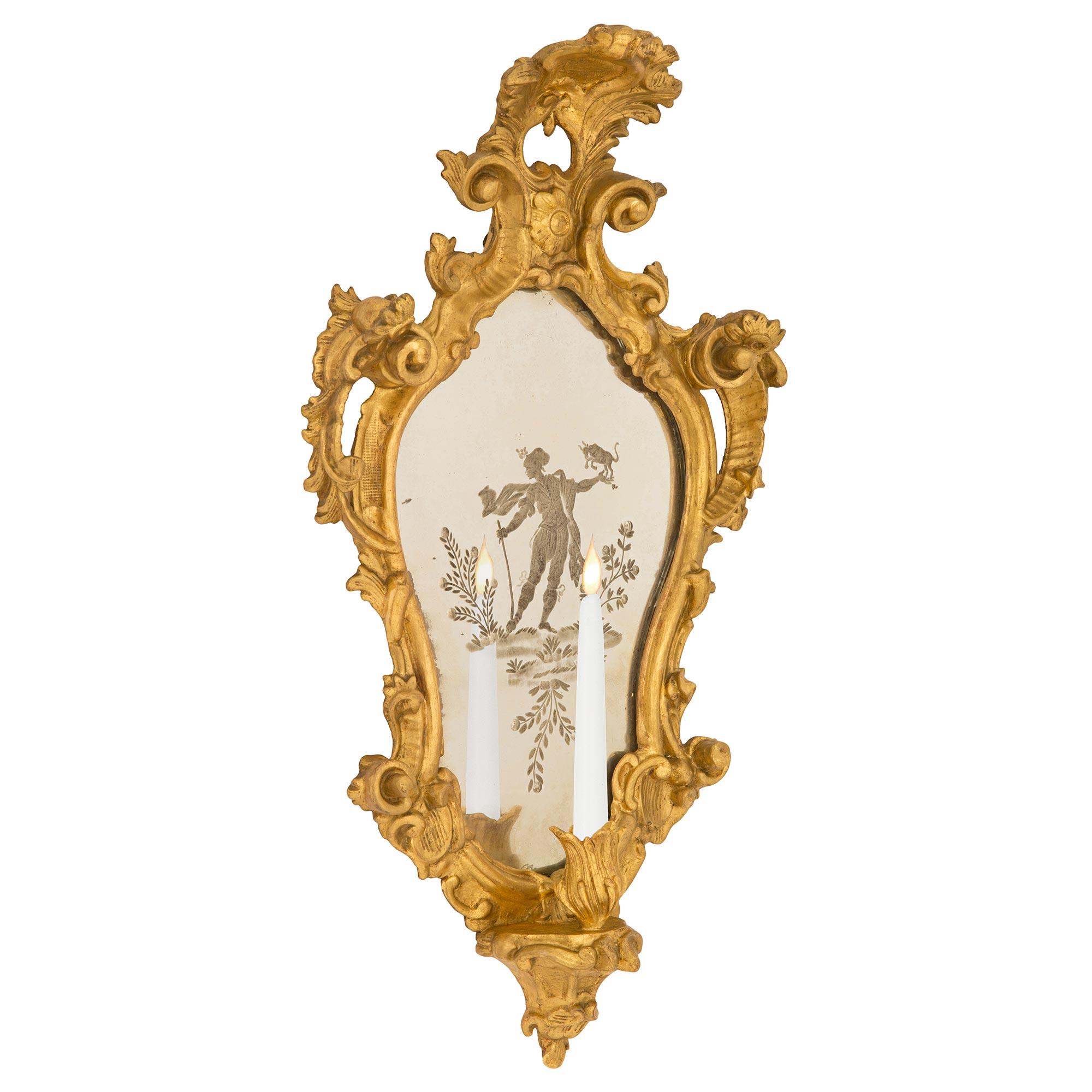 A wonderful true pair of Italian early 19th century Venetian st. giltwood and etched mirror sconces. Each beautiful single arm sconce displays a charming richly carved scrolled foliate arm at the base with striking wonderfully executed scrolled