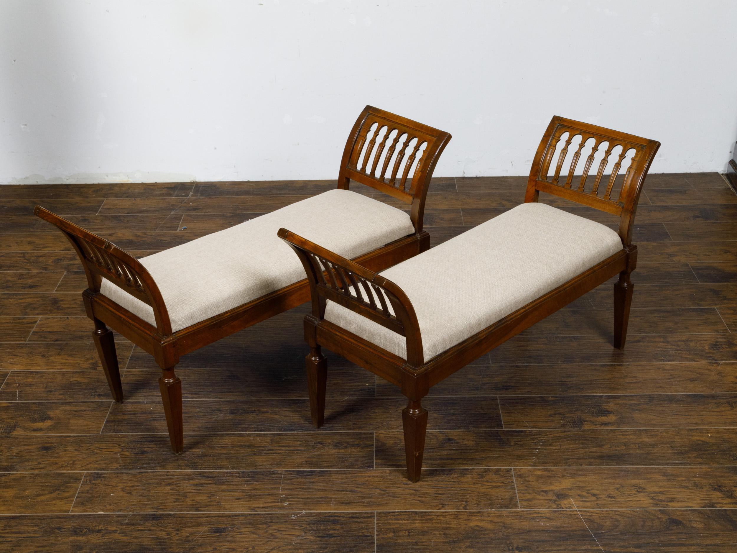 A pair of Italian walnut benches from the 19th century with out-scrolling side supports, tapered legs and new custom linen upholstery. This pair of Italian walnut benches from the 19th century effortlessly combines historic elegance with modern
