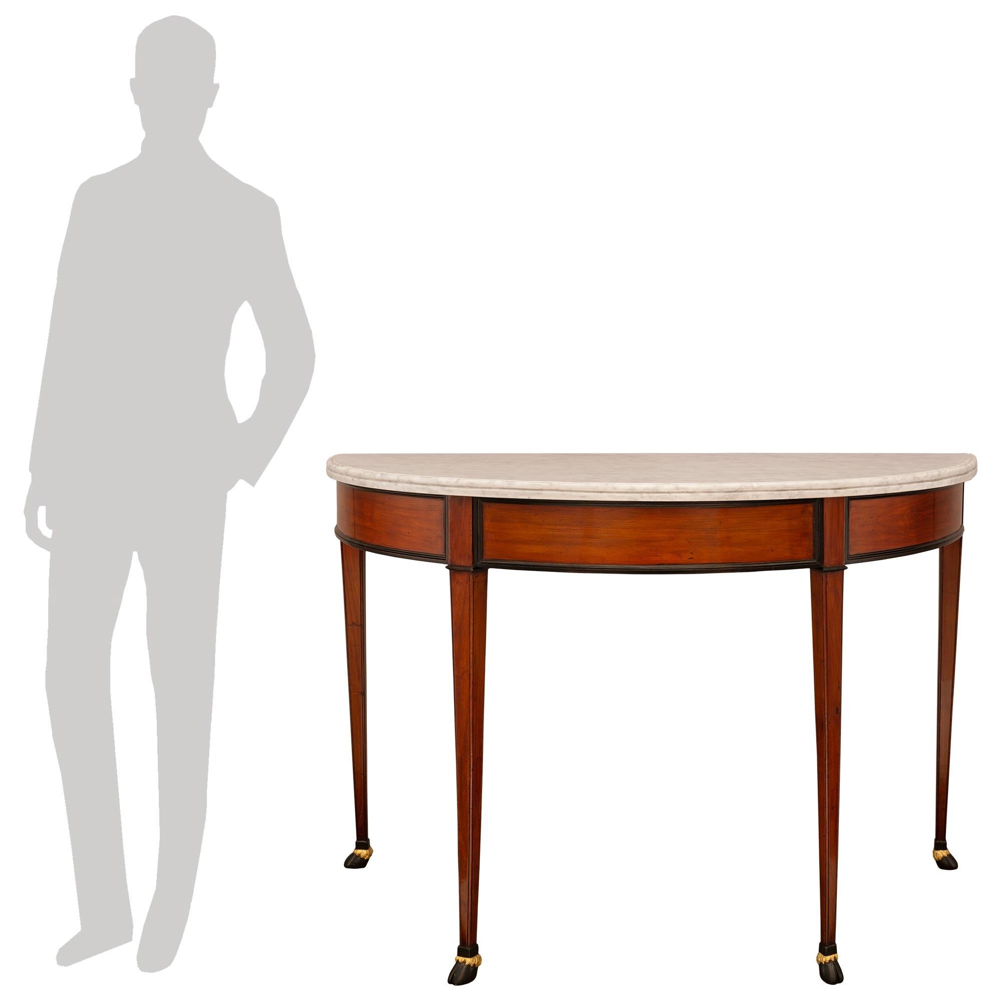Ein beeindruckendes Paar italienischer Konsolen aus dem 19. Jahrhundert im Stil Louis XVI aus Nussbaum, ebonisiertem Obstholz, Giltwood und weißem Carraramarmor. Jede attraktive, freistehende Demi-Lune-Konsole steht auf vier quadratischen,
