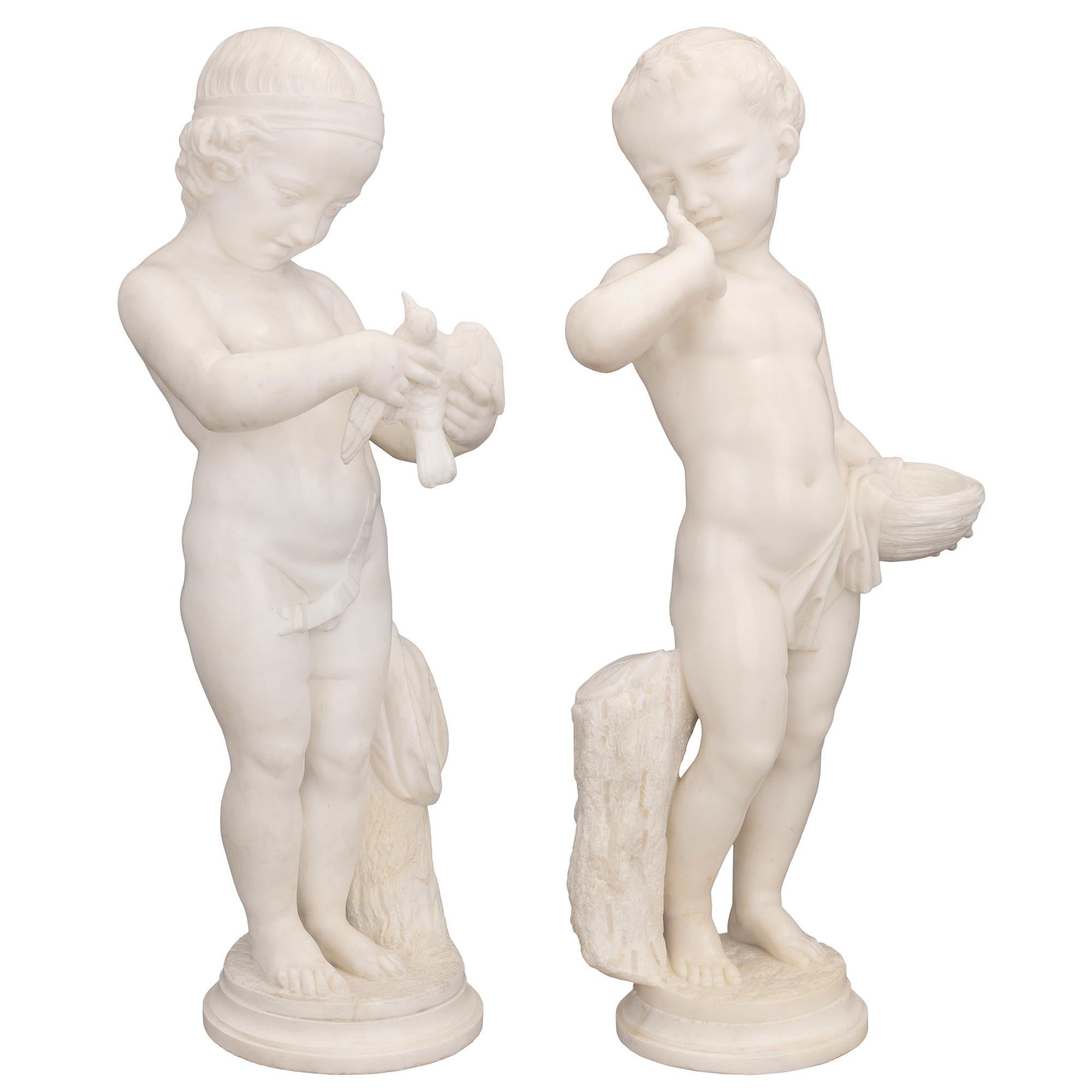 A most charming true pair of Italian 19th century white Carrara marble statues. Each statue is raised by a circular base with a fine mottled border and a wonderfully executed ground-like design. Above are the richly carved statues of a lovely young