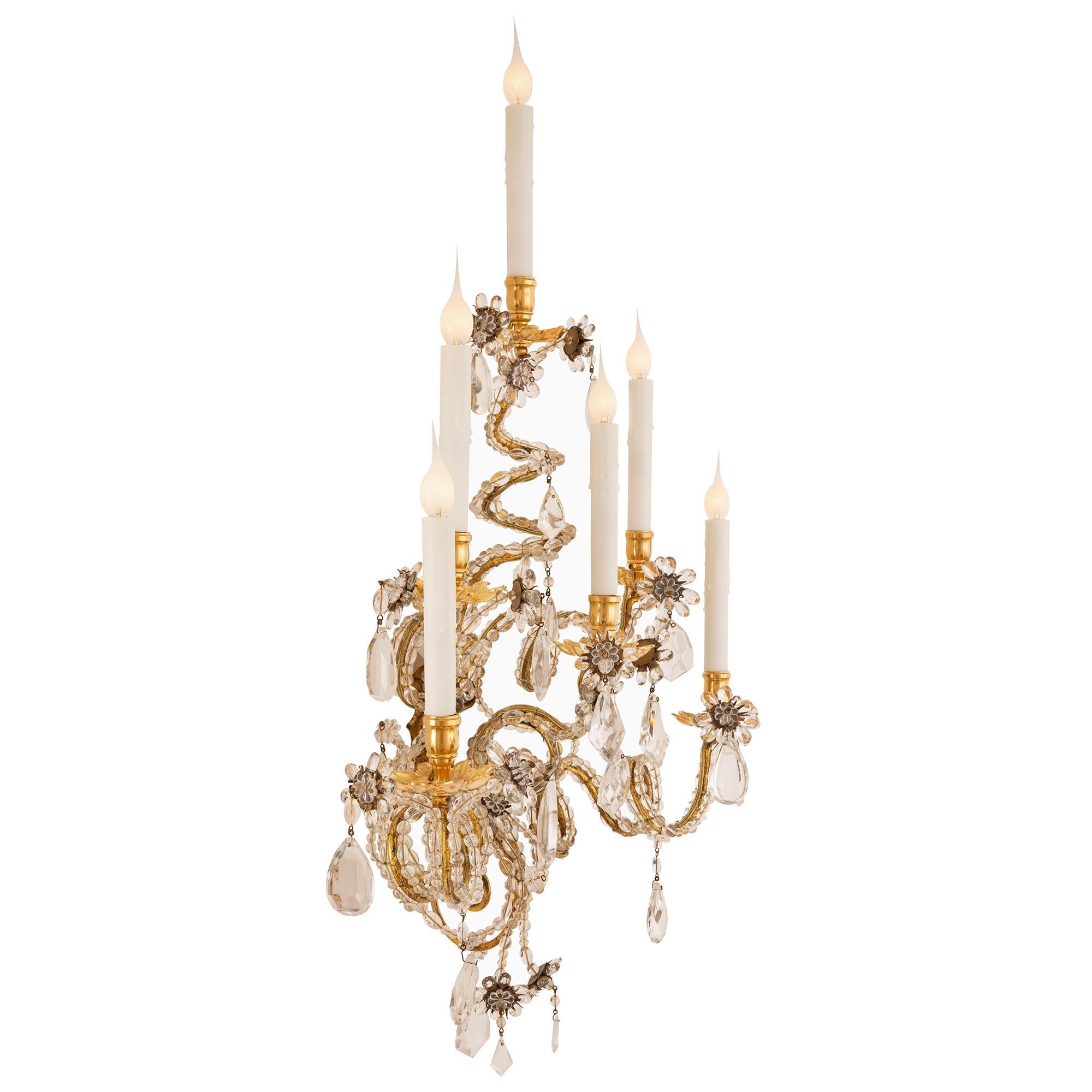 An outstanding and most decorative true pair of Italian turn-of-the-century gilt metal, ormolu, glass, and crystal sconces. Each six arm sconce is centered by a lovely charming crystal and beaded glass flower below the stunning scrolled twisted arms