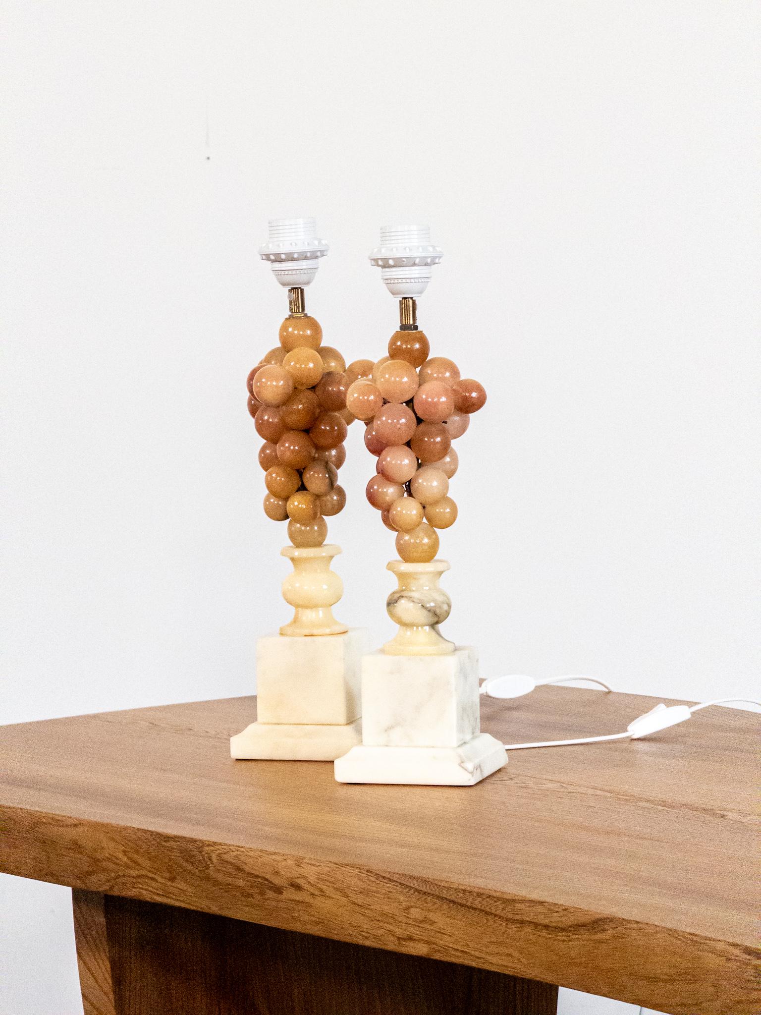 Una coppia unica e decorativa di lampade da tavolo della metà del secolo scorso con grappoli d'uva in alabastro splendidamente scolpiti nei toni caldi del miele, dell'ambra e del fard. Montate sulle classiche basi squadrate in alabastro, queste
