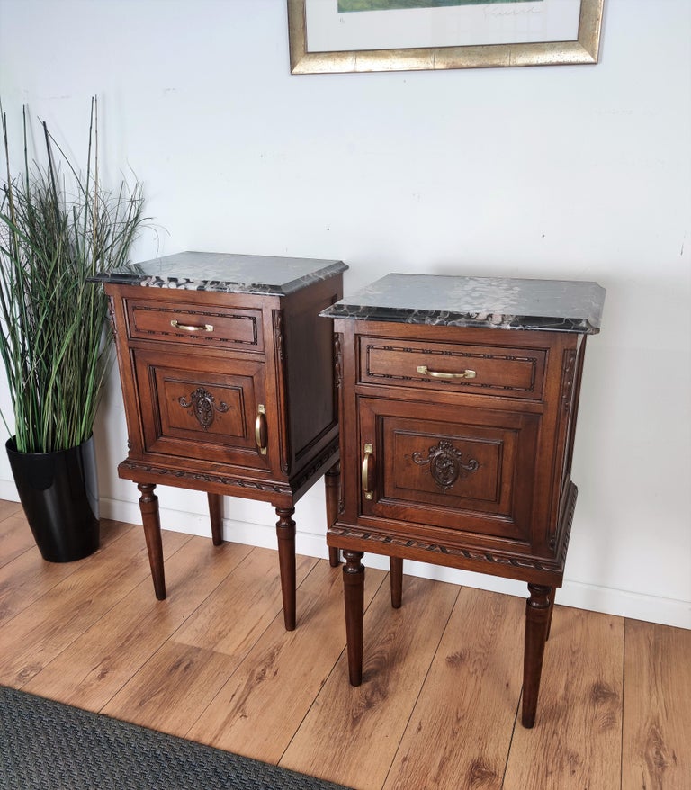 Pair of lovely Italian wood carved decorated night stands or side tables with beveled black marble top. The nightstands have a top carved framed drawer and door with front wooden carved classical flower and fruit decor with brass handles.
 