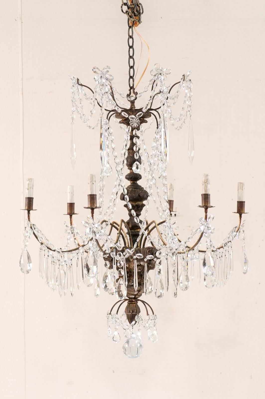 A pair of Italian early 20th century, six-light, crystal and wood chandeliers. This pair of antique Italian crystal chandeliers each features a decoratively carved central wood column, and a prominent splayed crystal waterfall top adorn with