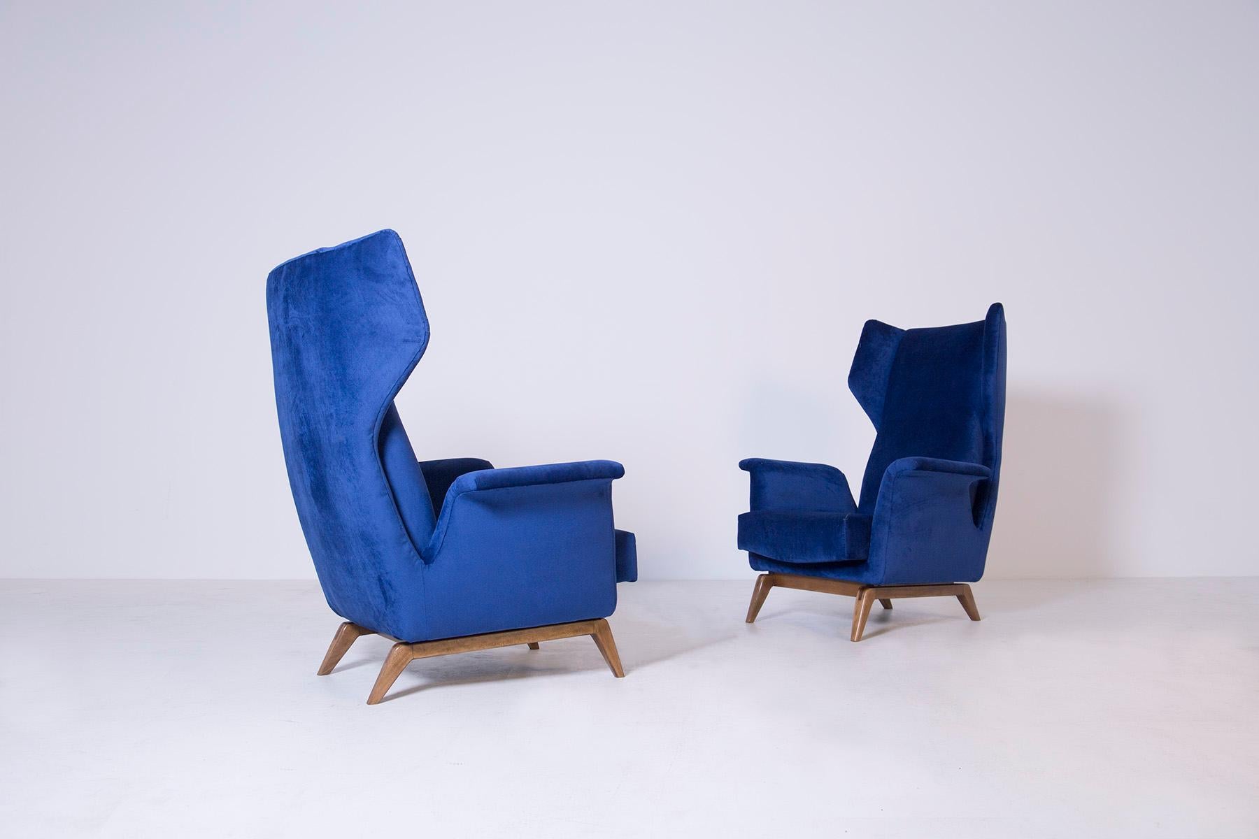 Elegant pair of armchairs from the Cassina manufacture of the 1950s. The armchairs have been restored and re-lined in blue velvet. The peculiarity of the armchairs is its wraparound back through two ears coming out of the body. Its wing shaped