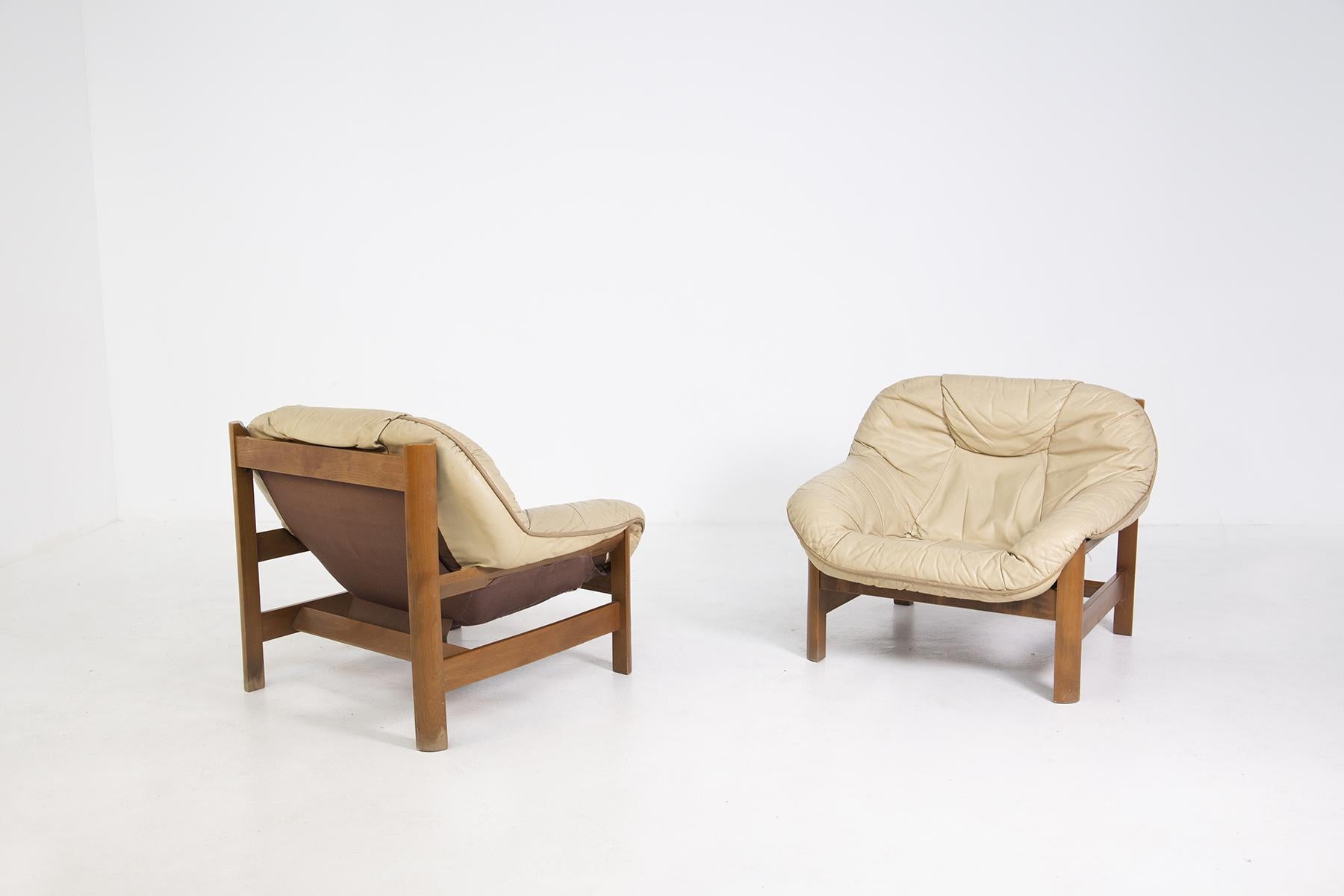 Pair of Italian-made armchairs from the 1960s.
The pair of armchairs is made with a wooden frame and an enveloping cushion covering both seat and back in beige leather.
The leather seat is so comfortable that it also envelops the armrests.
The