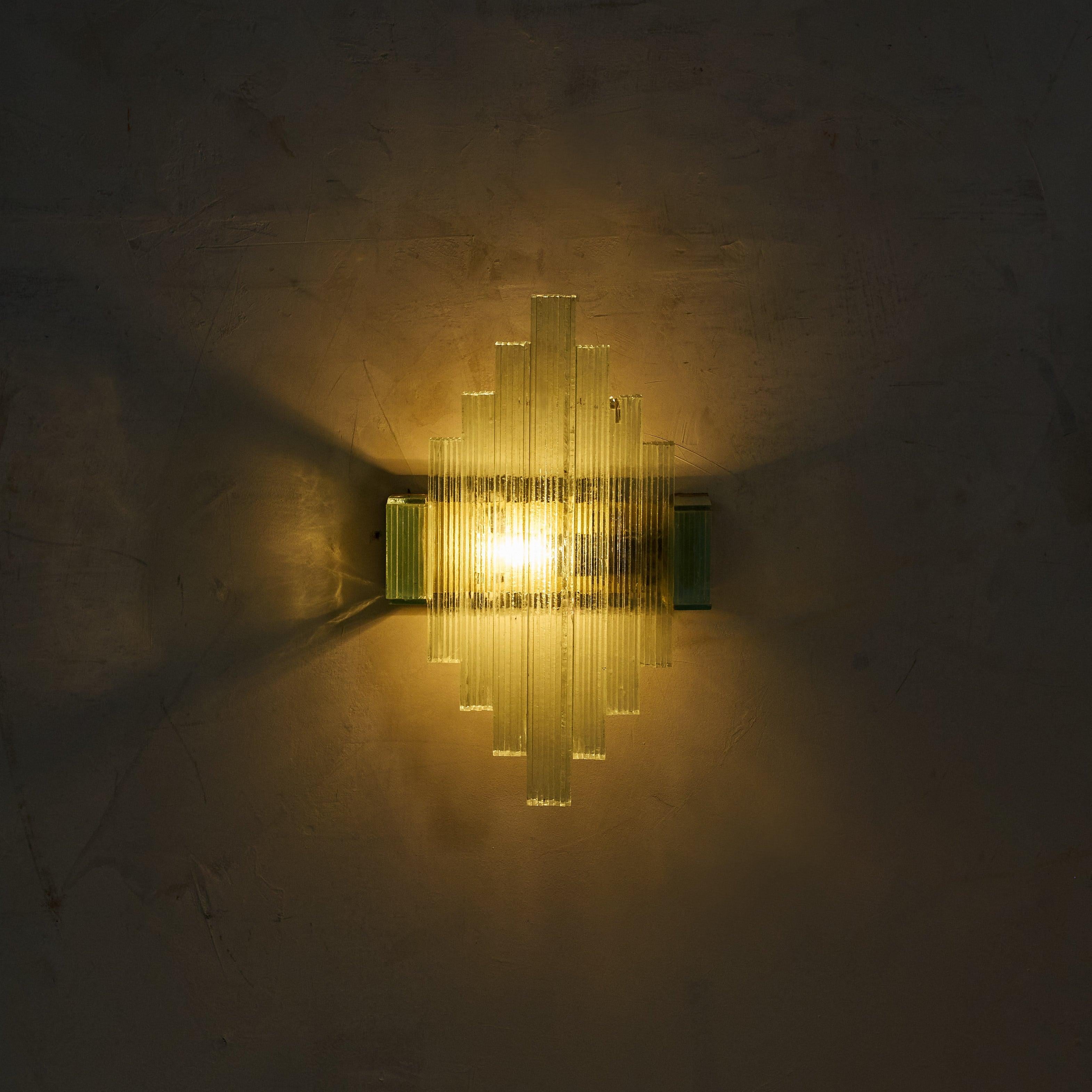With their stepped, geometric design and softly textured green glass, this pair of Italian sconces channels the Art Deco aesthetic through a 1960s lens. The architectural glass panels refract light in a captivating way, while the brass backplates