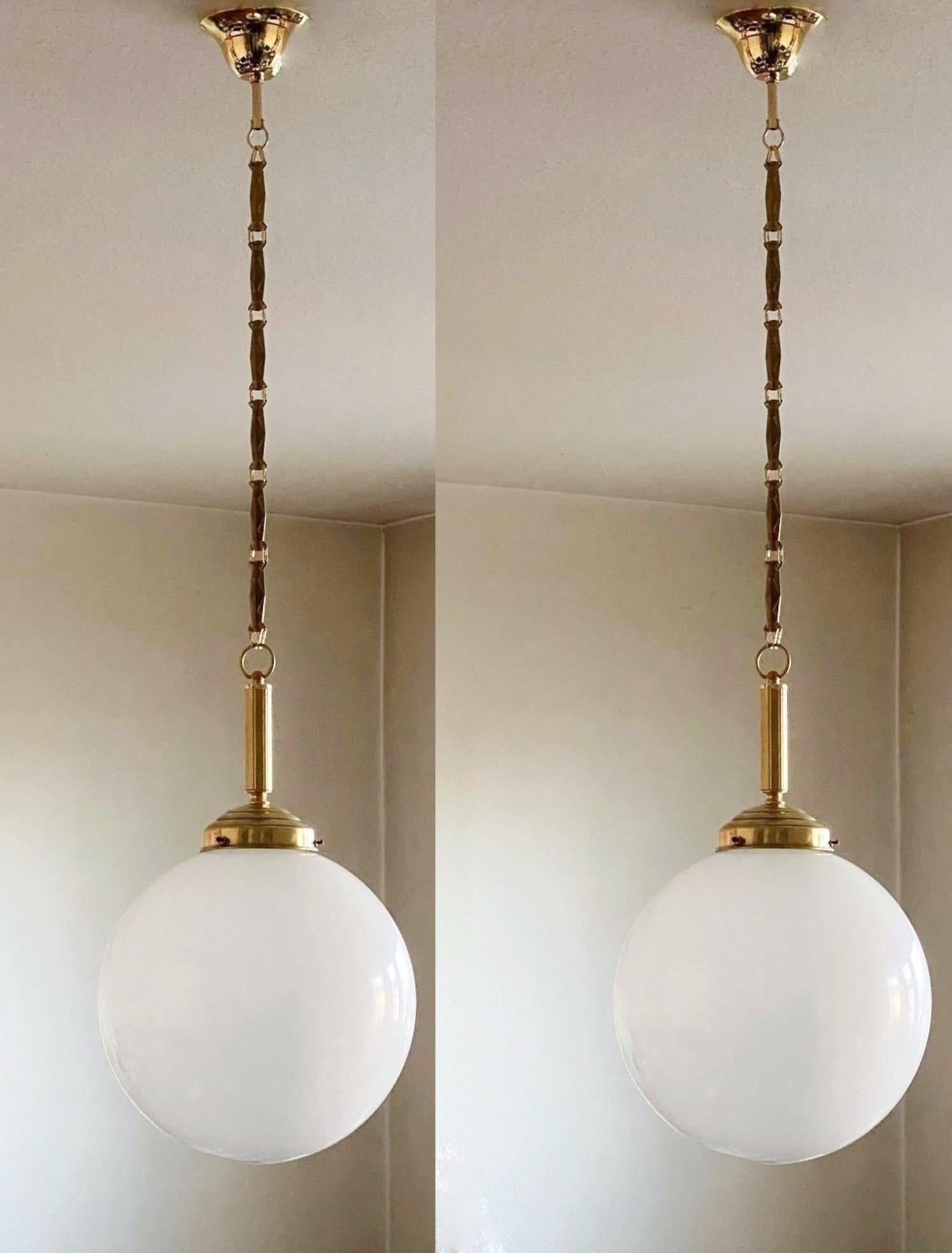Pair of  hand blown opaline glass ball pendant with brass mounts, chain and canopy, Italy, 1940s.
One porcelain Edison E-27 light socket for a large sized screw bulb up to 100W. Both pendants in very good condition,   no damages,
