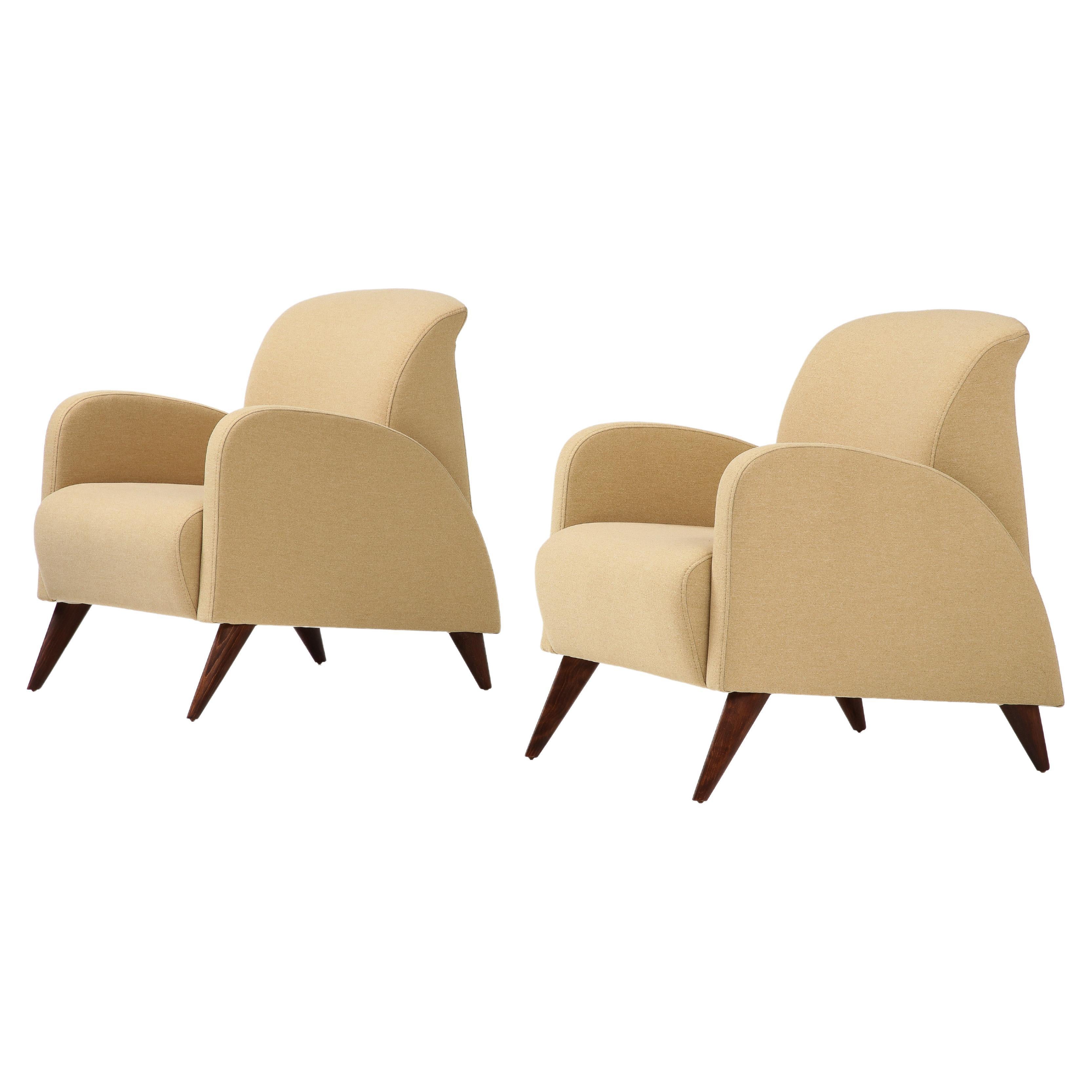 A pair of Italian Art Deco armchairs; the form highly sculptural and streamlined, highly indicative of the glamorous, stylized and dynamic Art Deco period, the seats supported on elegantly splayed walnut legs. Newly re-upholstered and re-finished in