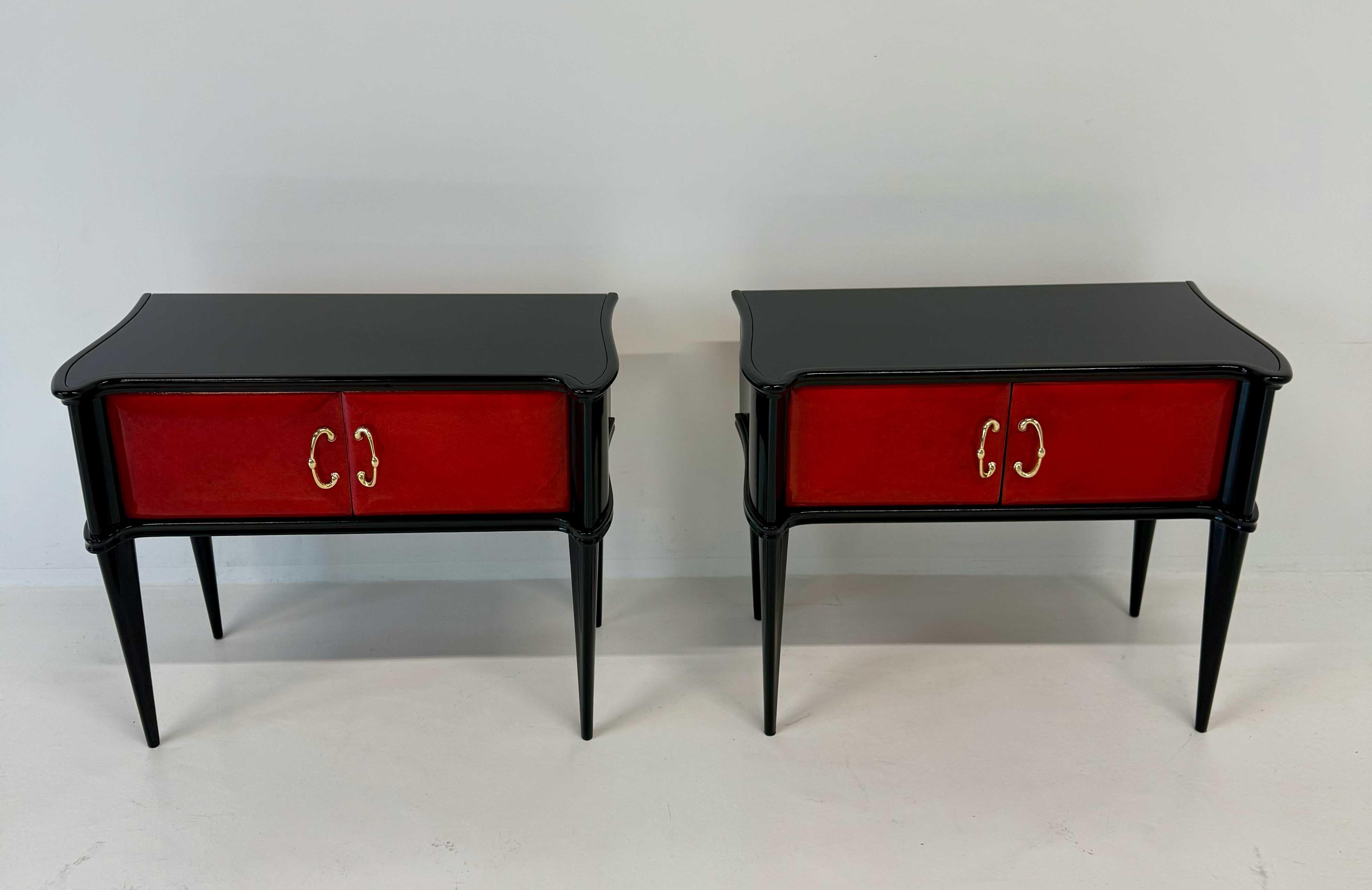Elégante paire de tables de nuit italiennes Art déco des années 1950, présentant des portes en parchemin rouge encadrées par une structure laquée noire épurée.
Les plateaux sont en verre noir, complétant parfaitement le contraste raffiné des