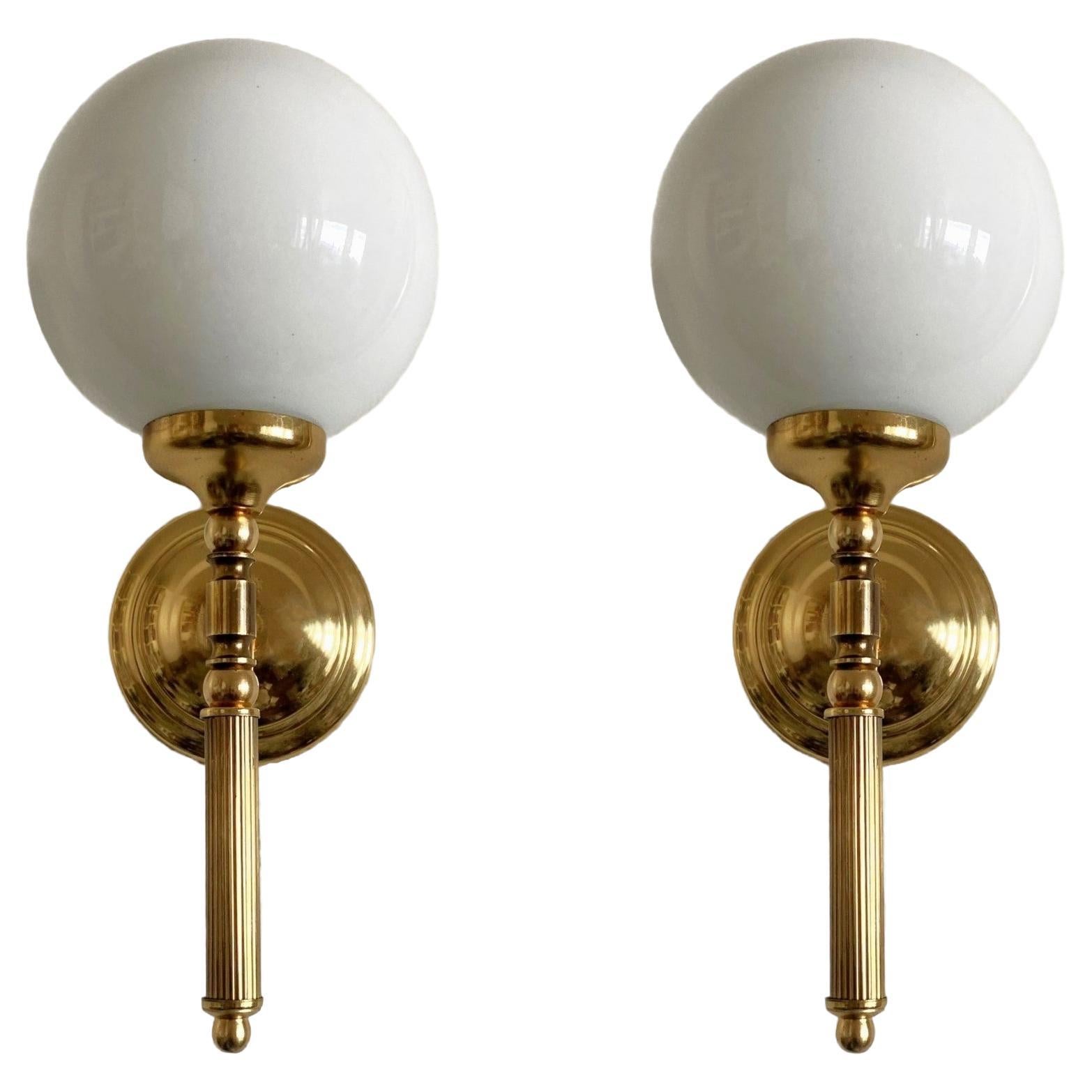 A pair of Art Deco torchiere wall lights n Maison Janson style, France, 1950s. Elegant design in gilt brass with hand-blown opaline glass ball globes. 
Both pieces in fine vintage condition, glass globes without chips or cracks, aged patina to