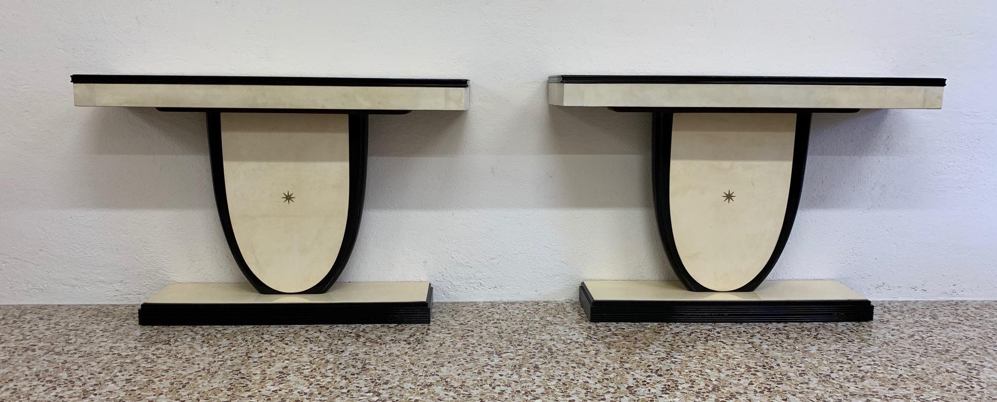 This pair of consoles was produced in Italy in the 1940s.
The front part of the base and tops are covered with parchment leather with black lacquered profiles, while the central detail is a brass star.