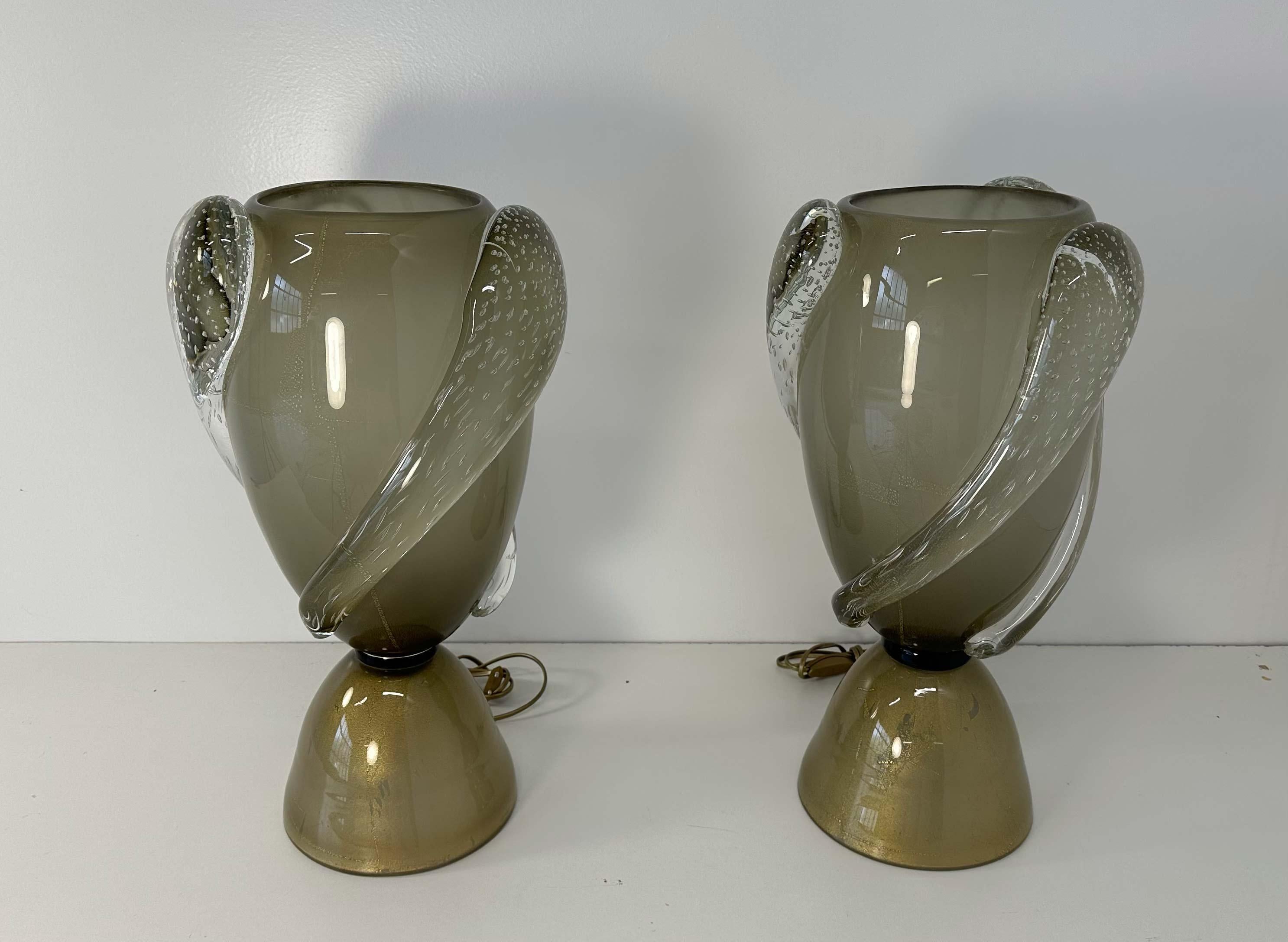 Questa coppia di lampade a vaso in stile Art Déco è stata prodotta in Italia negli anni 2000. 
Sono completamente in vetro di Murano grigio con piccoli pezzi di foglia d'oro all'interno. 
