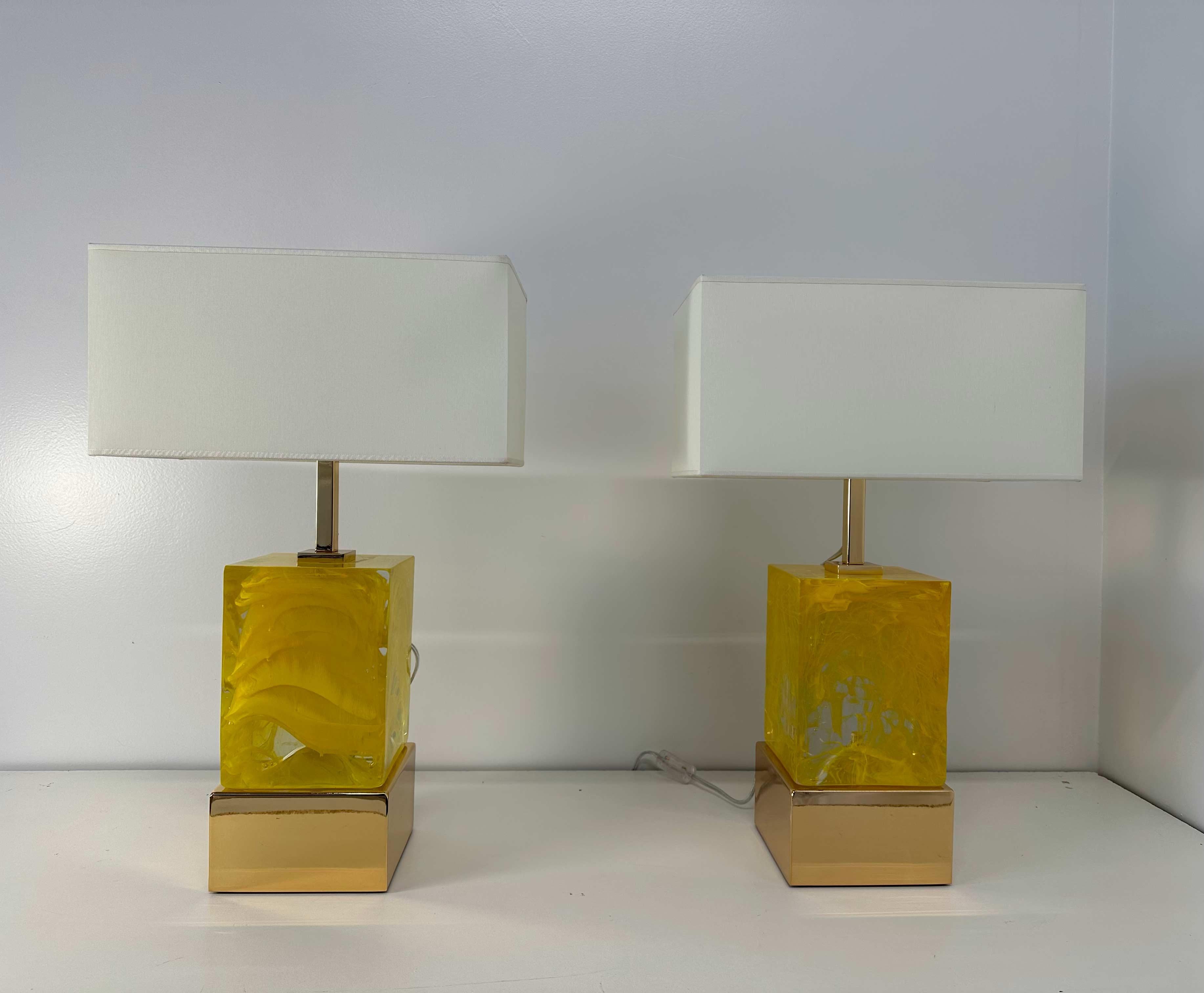 This pair of Art Deco style lamps was produced in Murano in the 2000s. 
The base and the upper part are in gold galvanized brass, while the central body is a transparent and yellow Murano glass cube. The Lampshade is included and it is white and