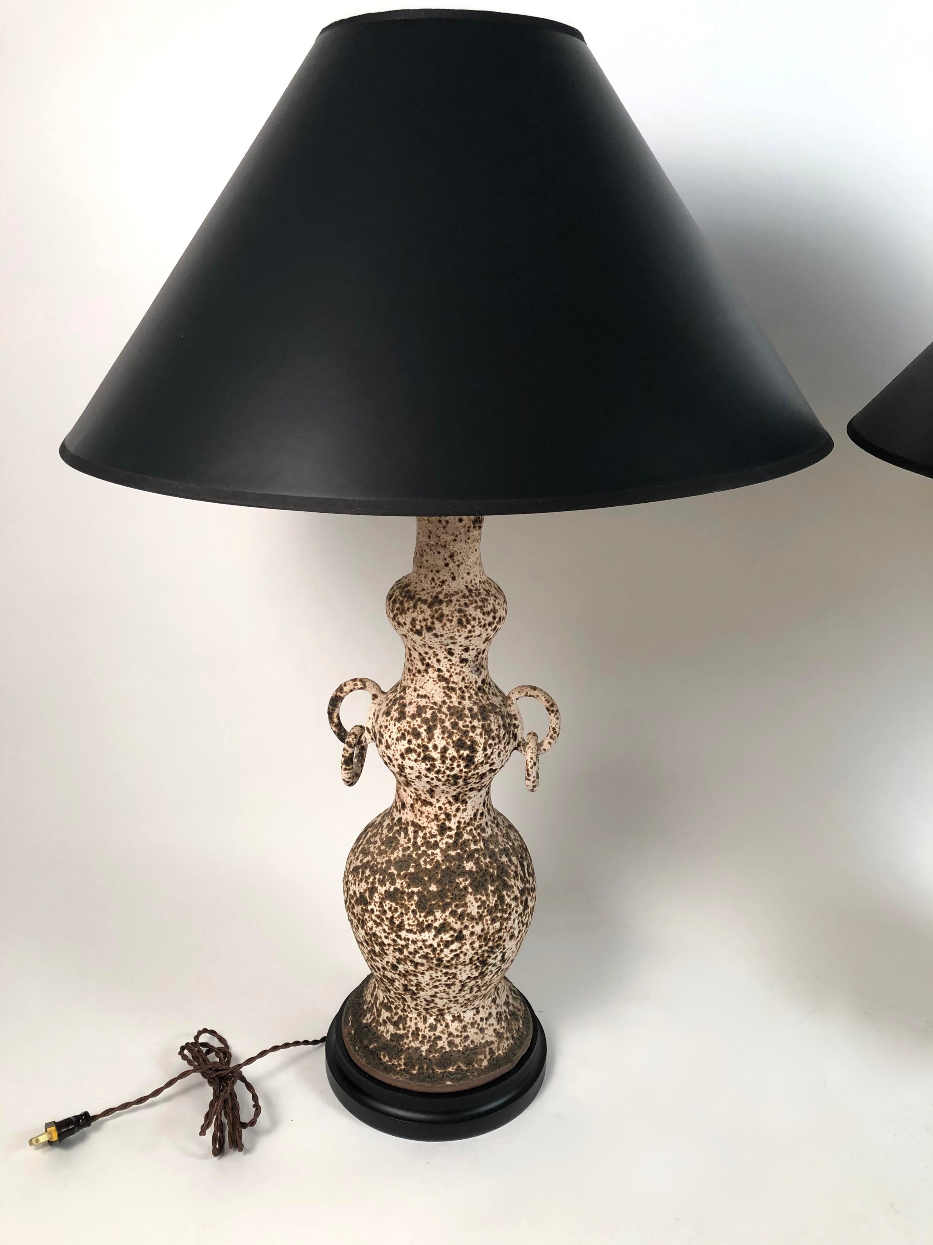 An unusual and stylish pair of Italian art pottery lamps, in the manner of Guido Gambone, each of triple gourd form with rings, mounted on black painted bases, with new wiring and electrical fittings. Shades available, if desired.