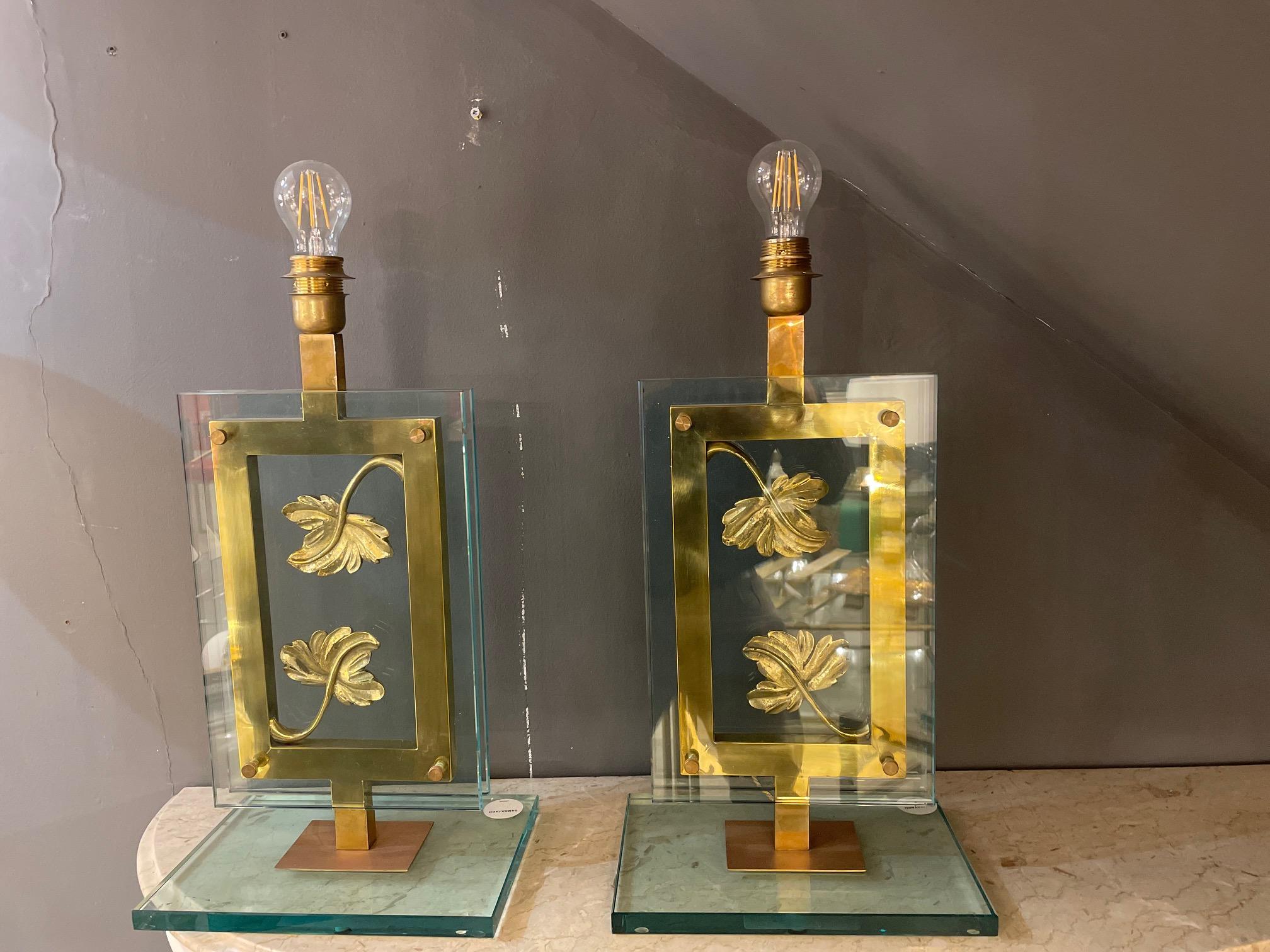 A pair of Italian artistic table lamps in brass and glass. The centre of the lamp supports two floating cast bronze leaves encased by rectangular glass on both t front and back of the lamp creating a framed foliage art piece.