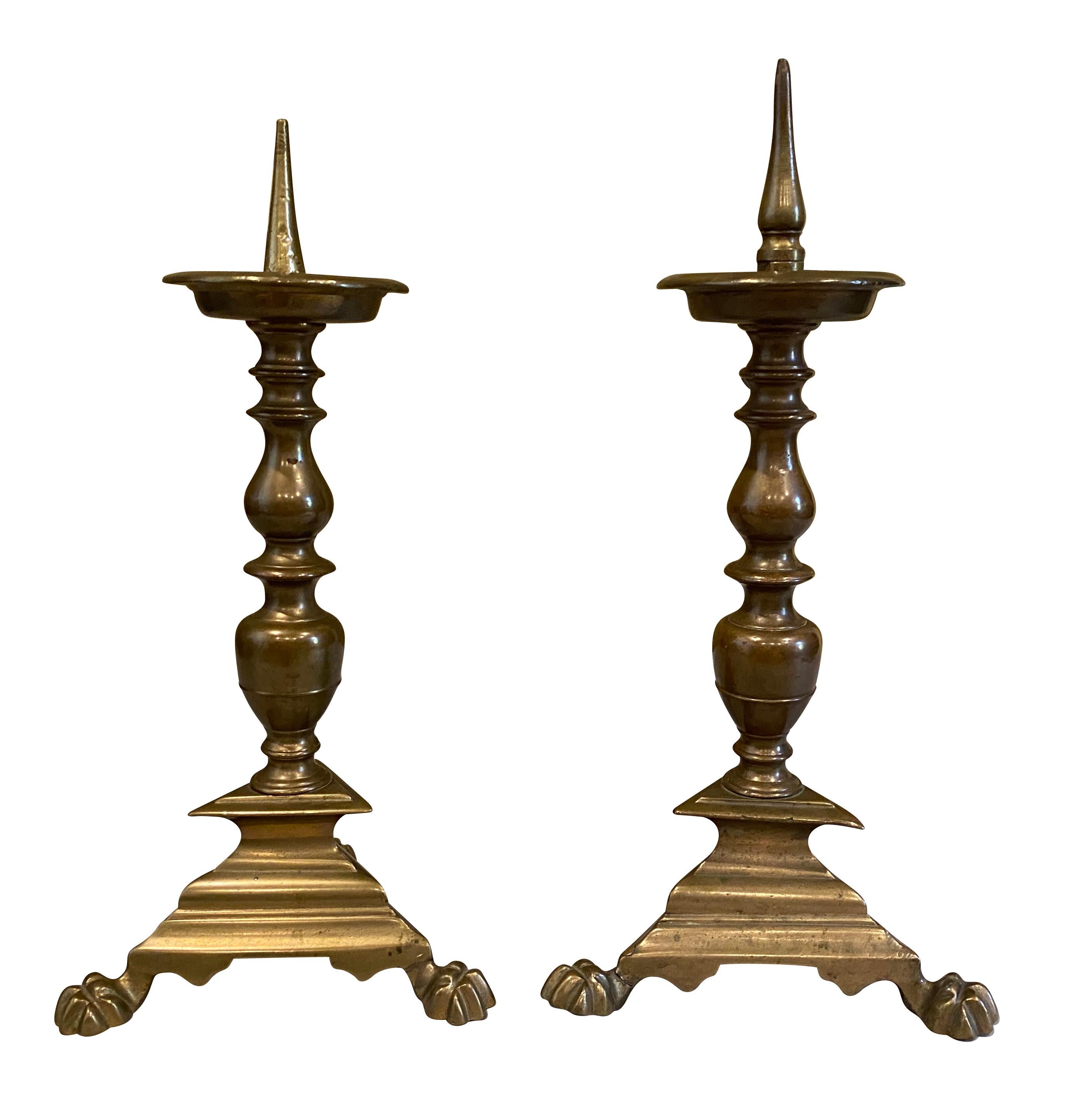 Typical form with candle pricket over a baluster form support and ending on a triangular base with paw feet.