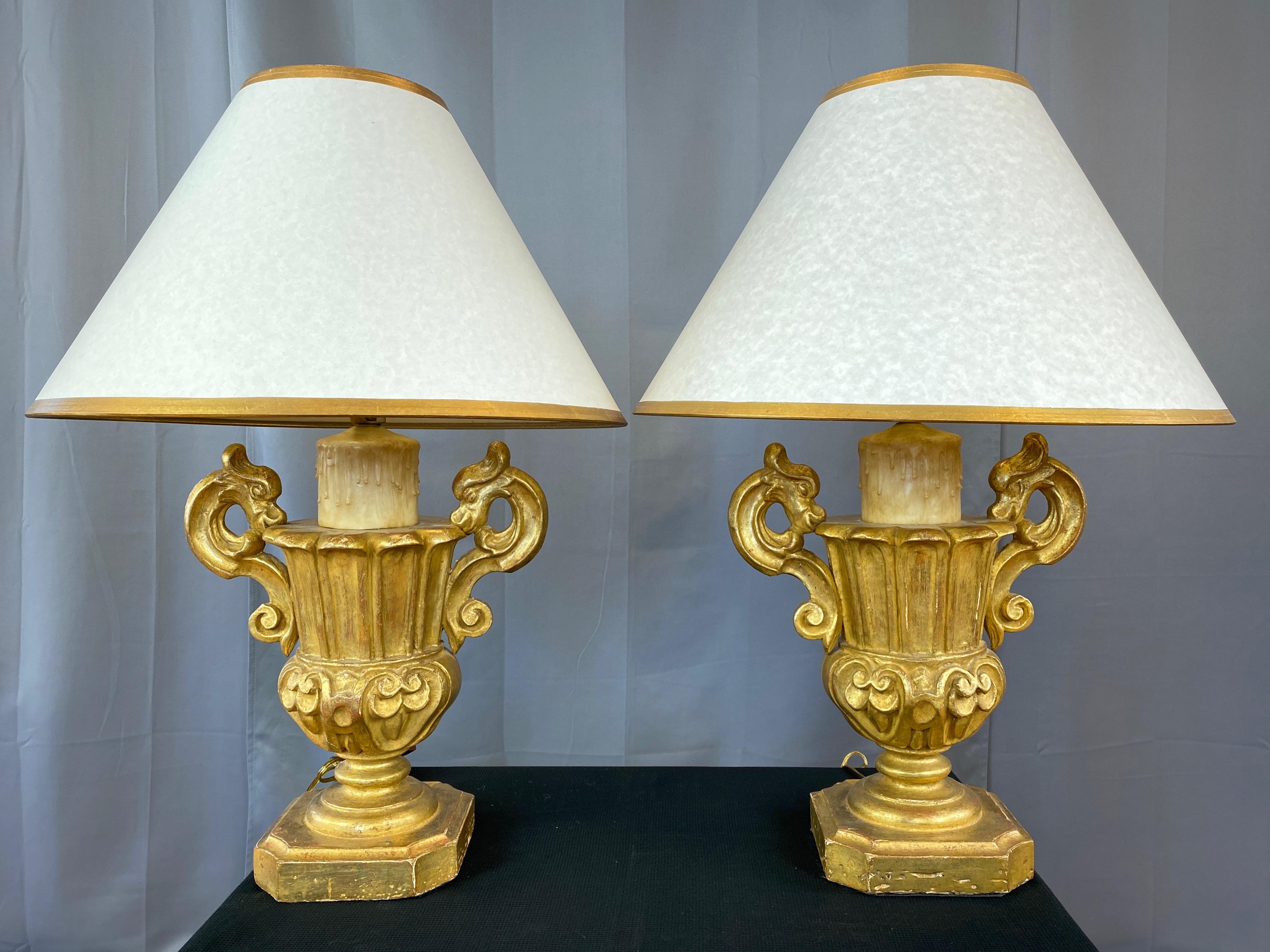 A dramatic and commanding pair of 1930s Italian Baroque Revival giltwood urn form table lamps with faux candle topper and custom shade.

Exquisitely carved wood body distinguished by elegant stylized serpent handles and deep-relief details