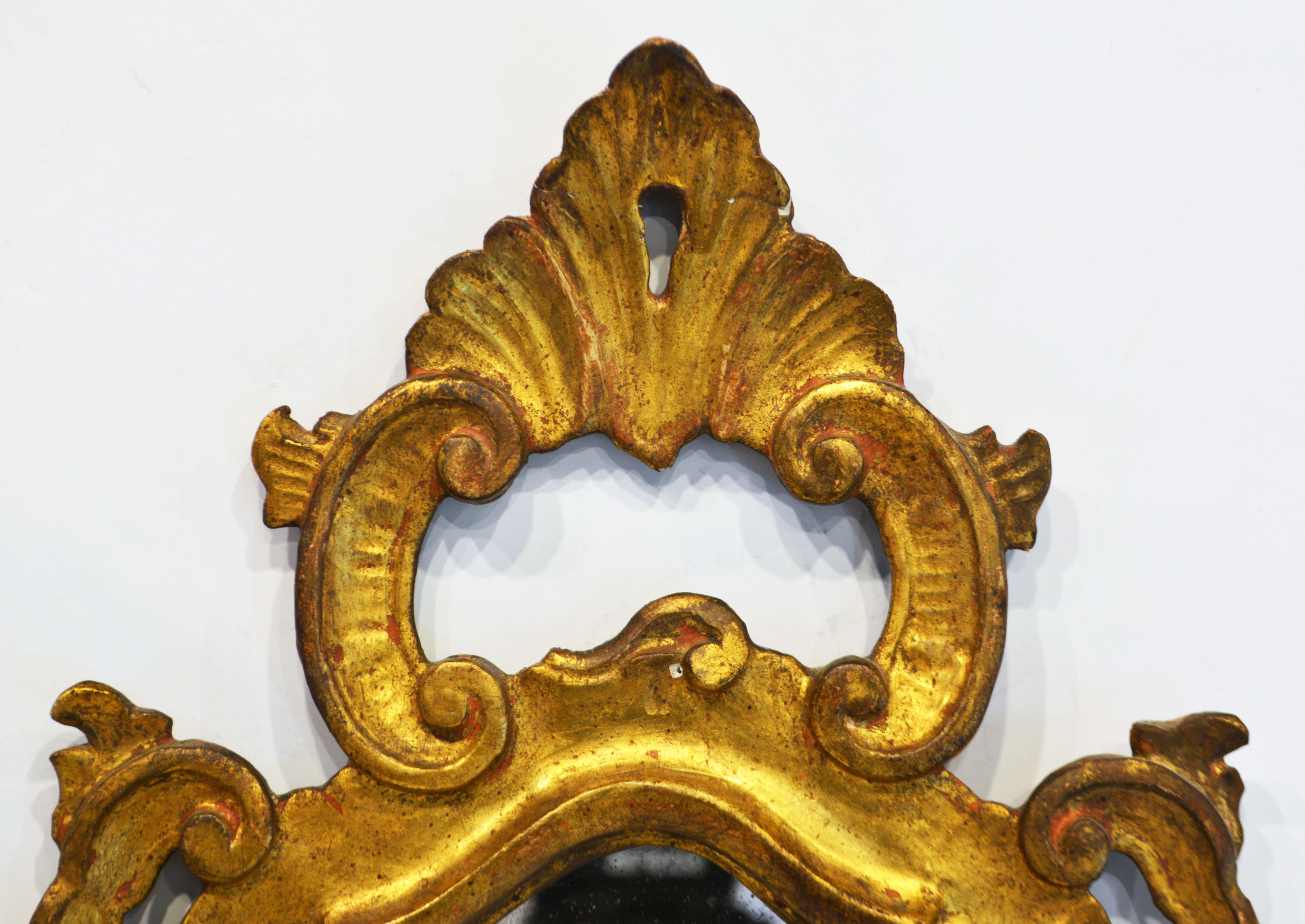 This pair of Italian carved giltwood mirror sconces represent an elegant fusion of the baroque and the later rococo style. They retain their old mirrors framed in exquisitely carved giltwood with shell crest and foliate scrolls. Each of the sconces